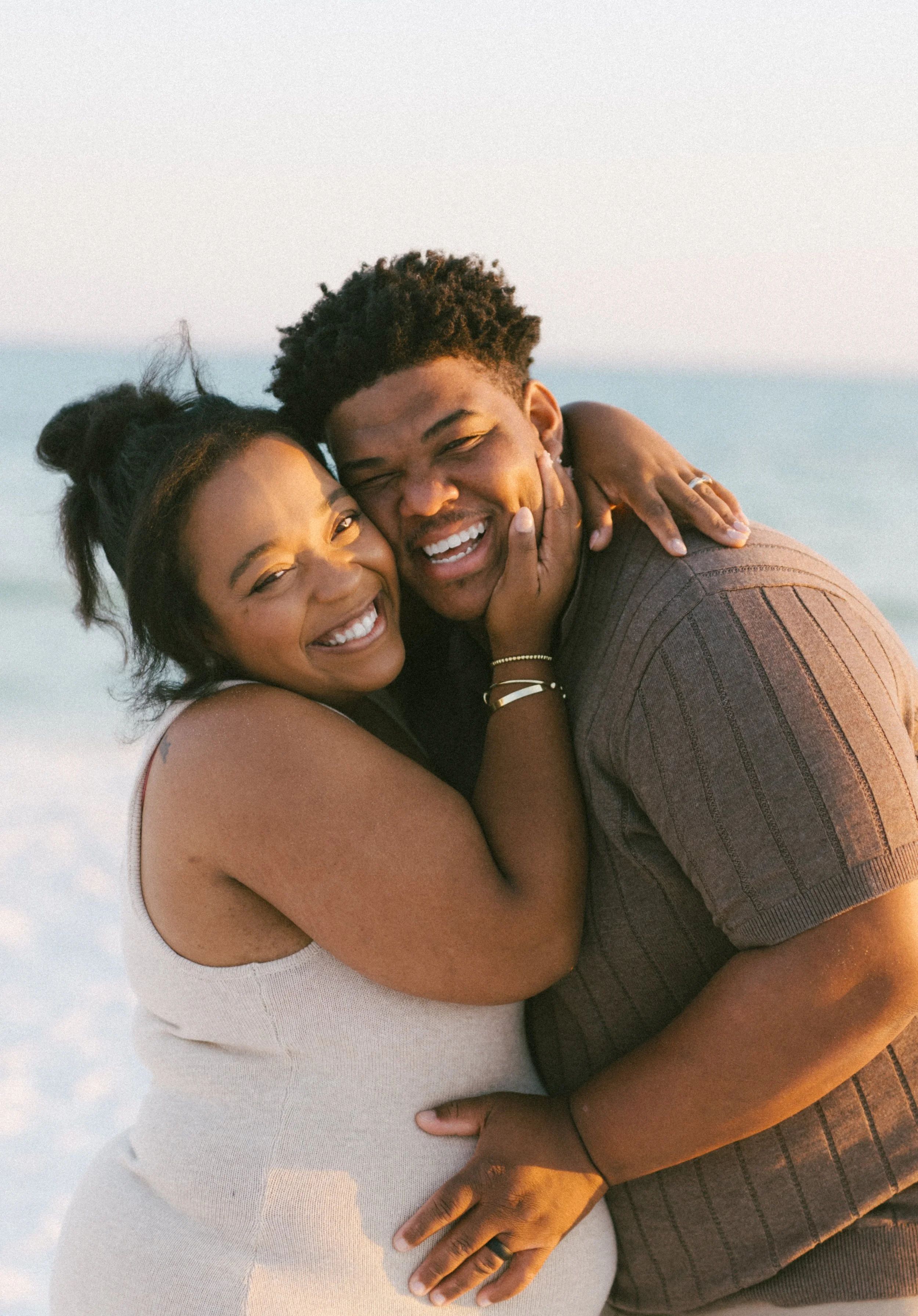 Smiling couple hugging on the beach at sunset, embracing each other closely.