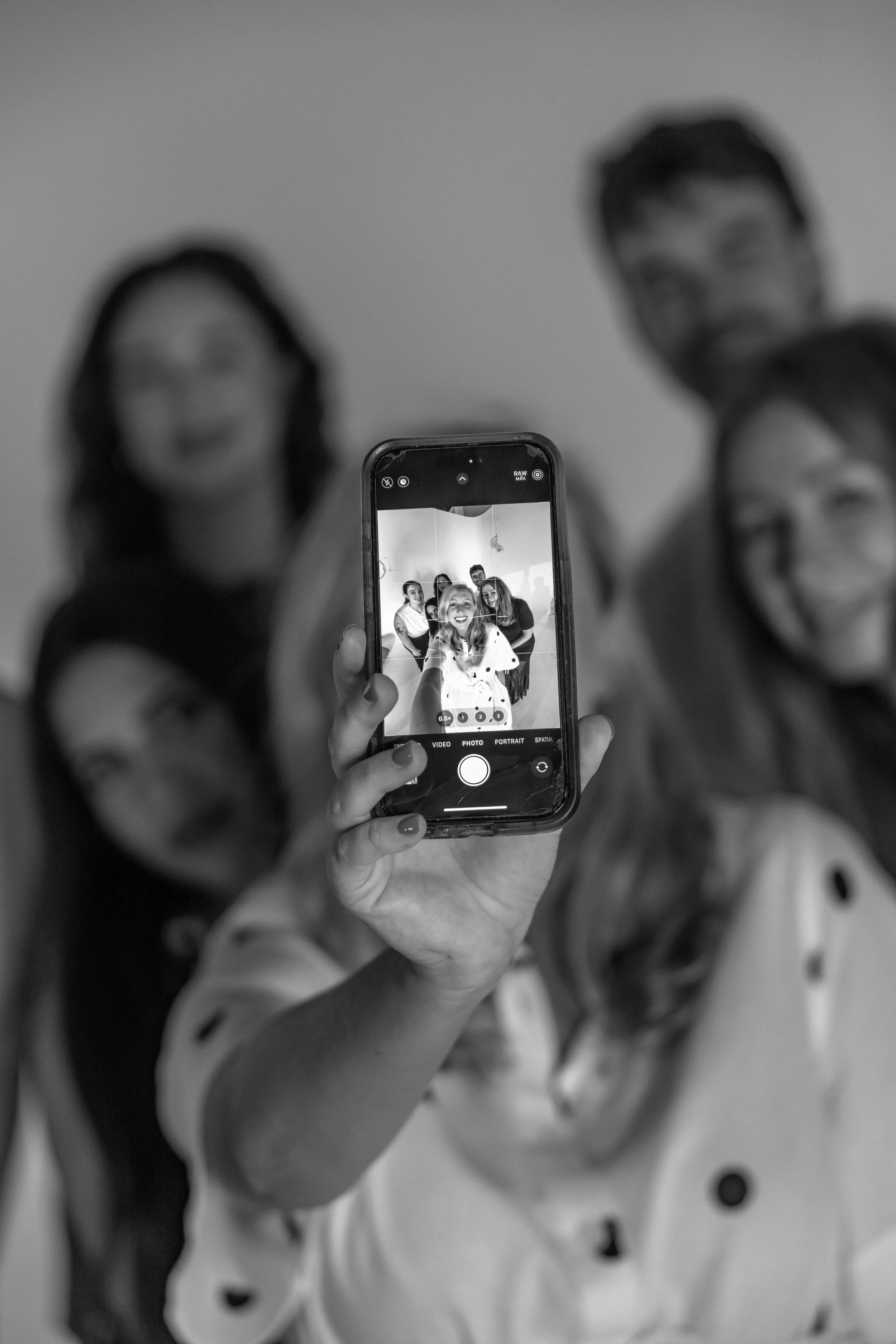A group of children pose for a photo, with some smiling and others making funny faces, while a person in the foreground captures the moment with a smartphone.
