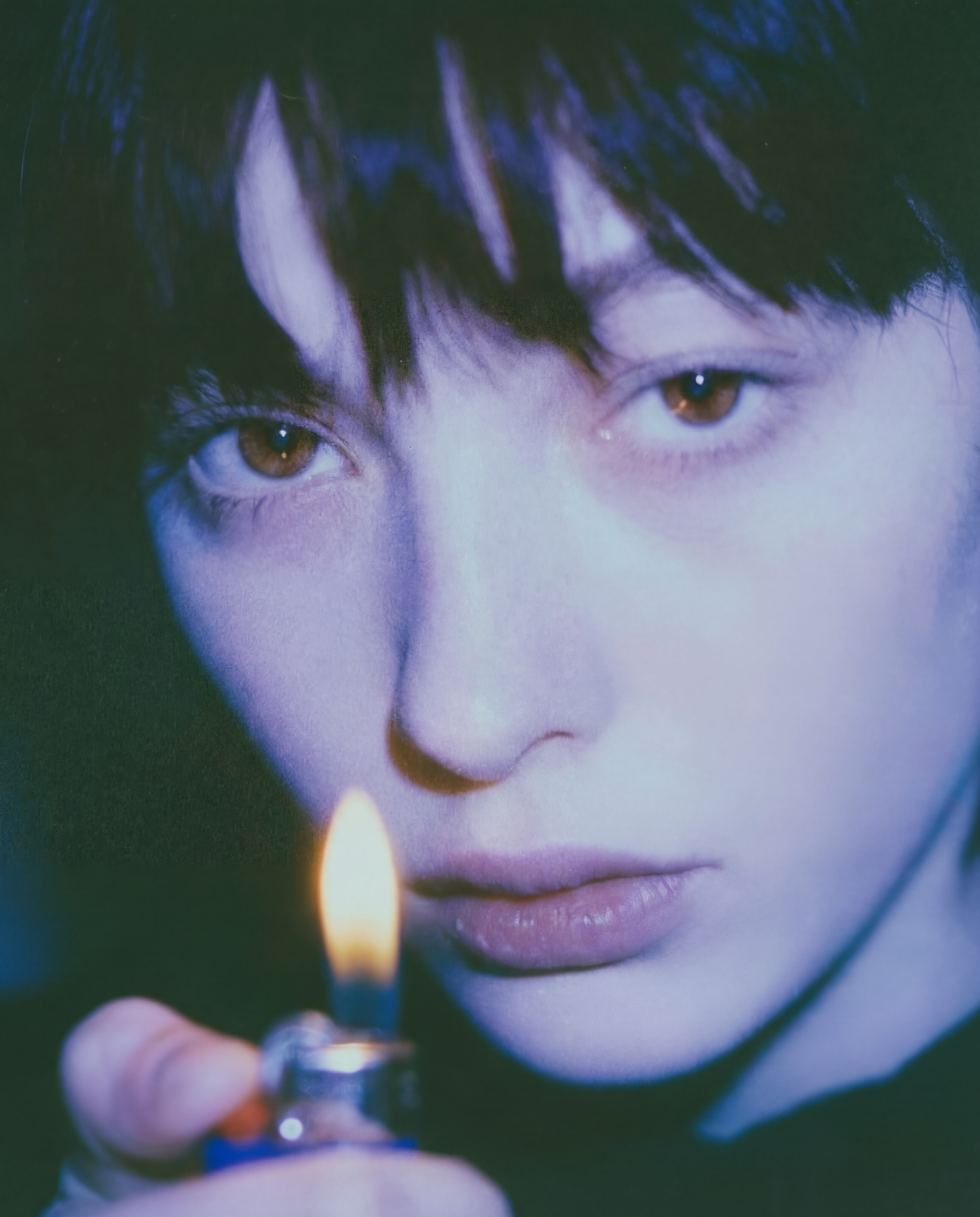 Close-up of a young person's face with brown eyes, holding a lighter with a flame near their face.