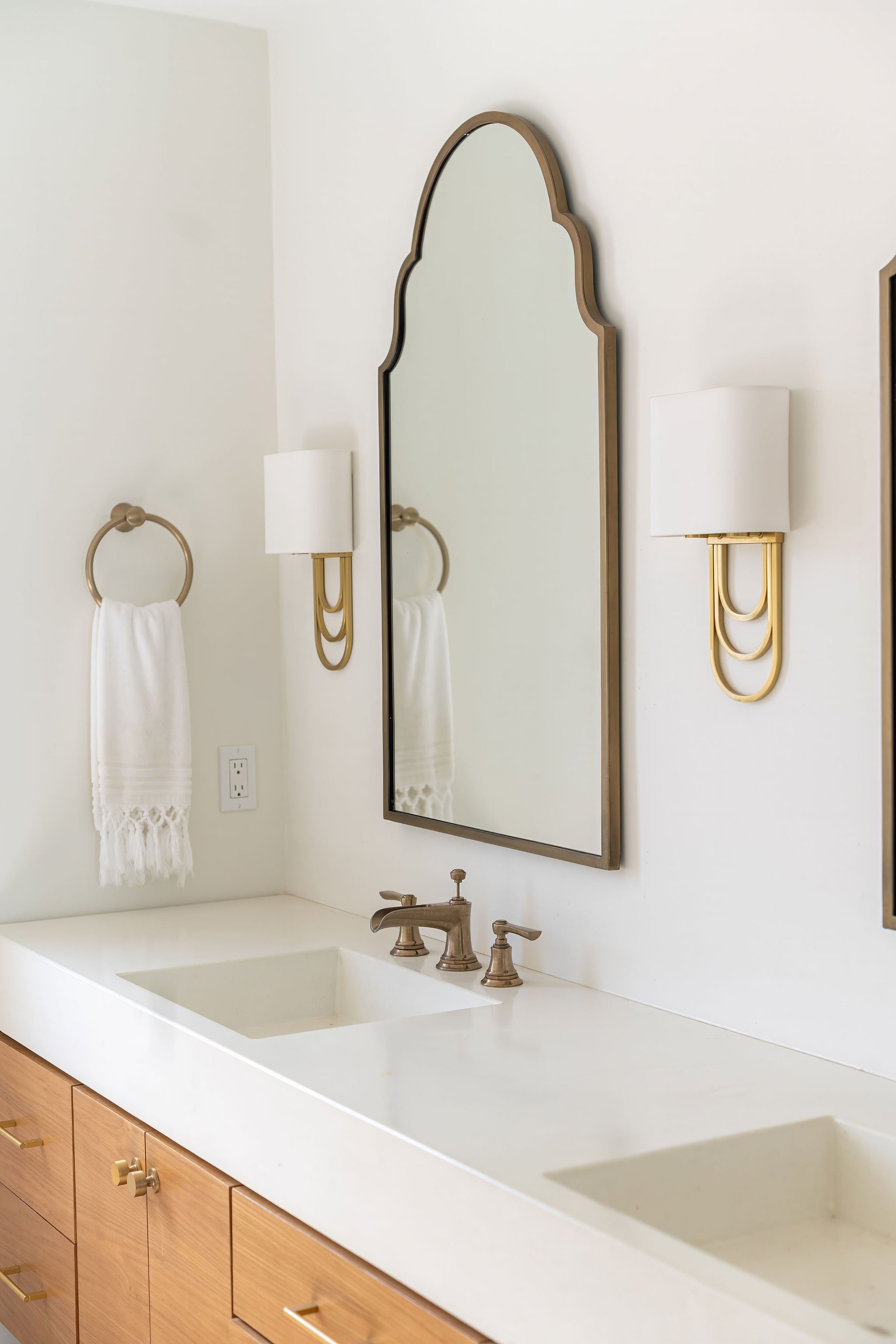 Modern bathroom vanity with a double sink, large mirror, gold wall sconces, a towel ring with a white towel, and wooden cabinets.