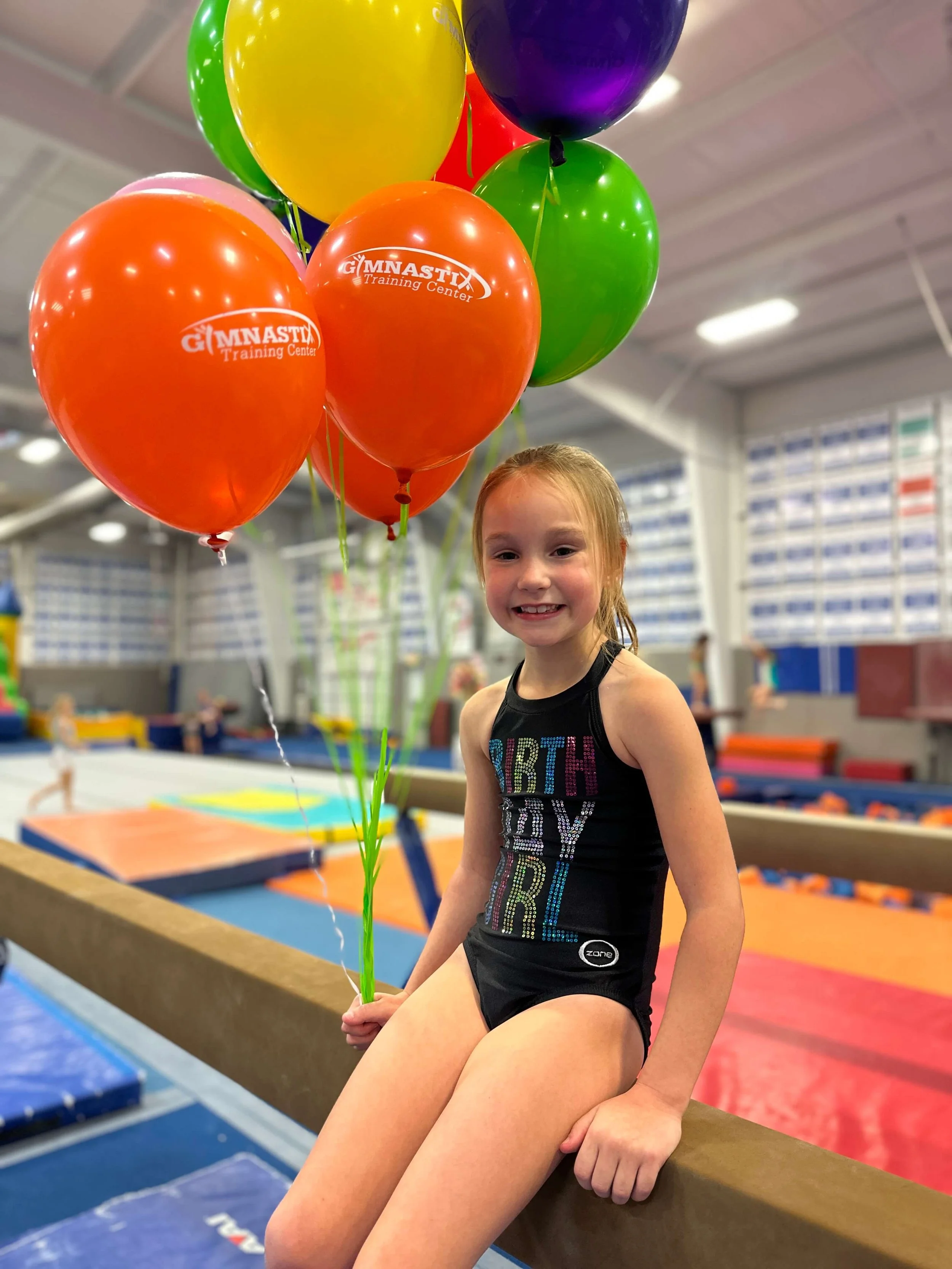 girl sitting on balance beam with birthday balloons