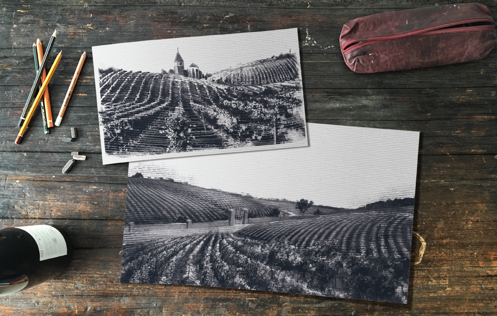 Black and white illustration of a vineyard with rolling hills, trees, and a church with a steeple and bell tower in the background, laying on a weathered wooden surface with art supplies nearby.