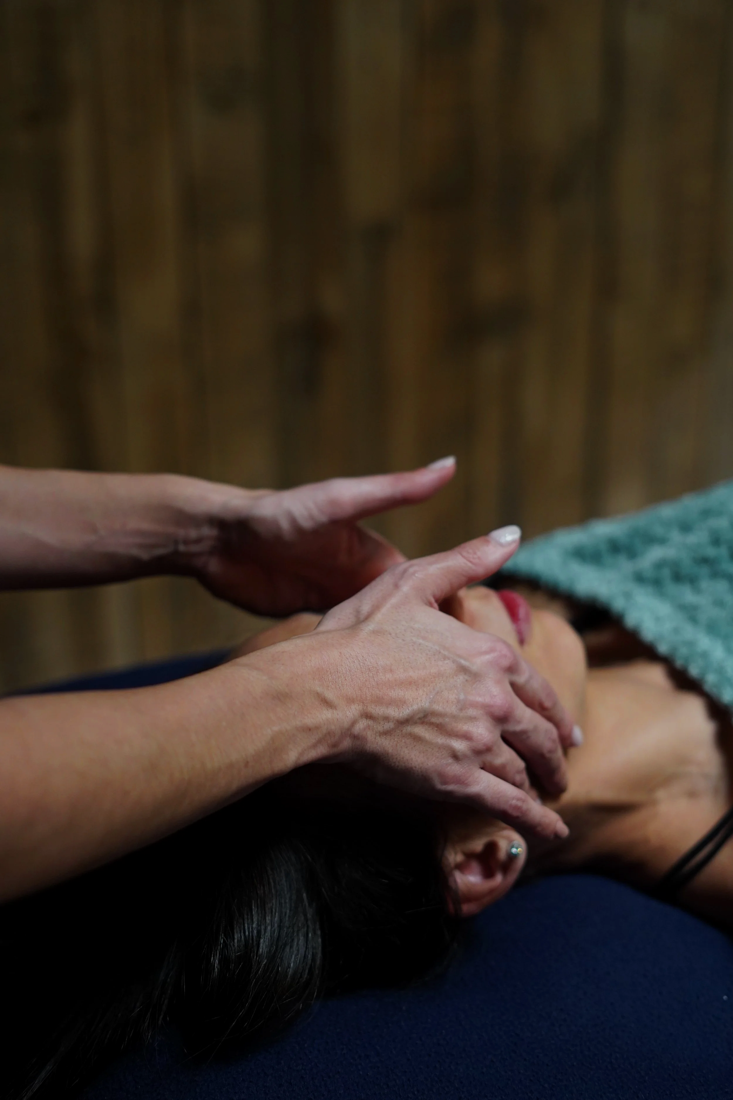 Une personne reçoit un massage, allongée sur le ventre, avec une main qui masse son dos. La personne a de longs cheveux noirs et porte un maquillage rouge à lèvres. La scène semble se dérouler dans un cadre chaleureux.
