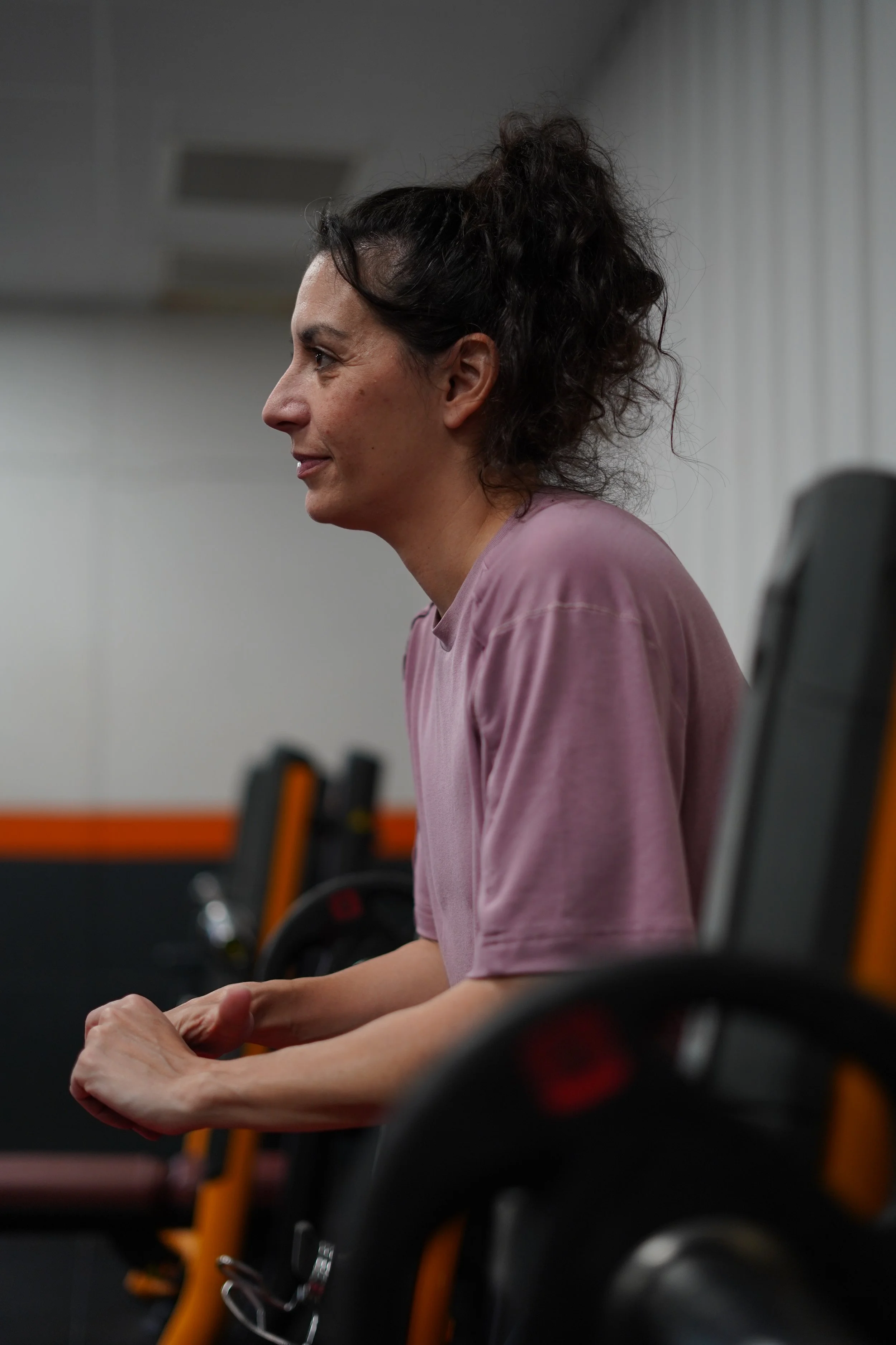 Une femme assise lors d'une séance d'entraînement ou de physiothérapie, concentrée avec ses mains jointes, dans un environnement intérieur avec des équipements de gym.