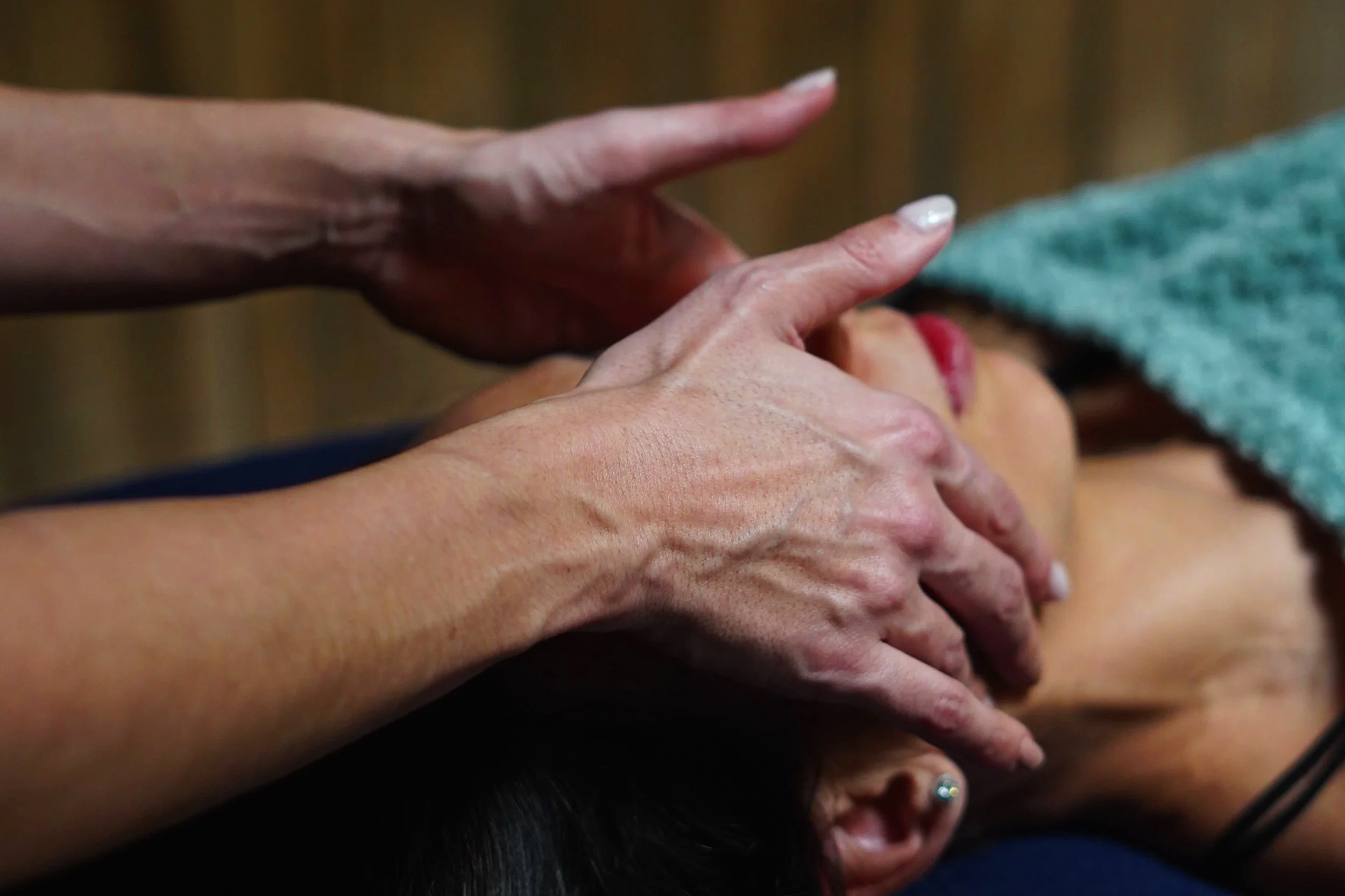 Une personne reçoit un massage ou une pression sur le visage, avec plusieurs mains appliquant une pression sur une autre personne allongée.