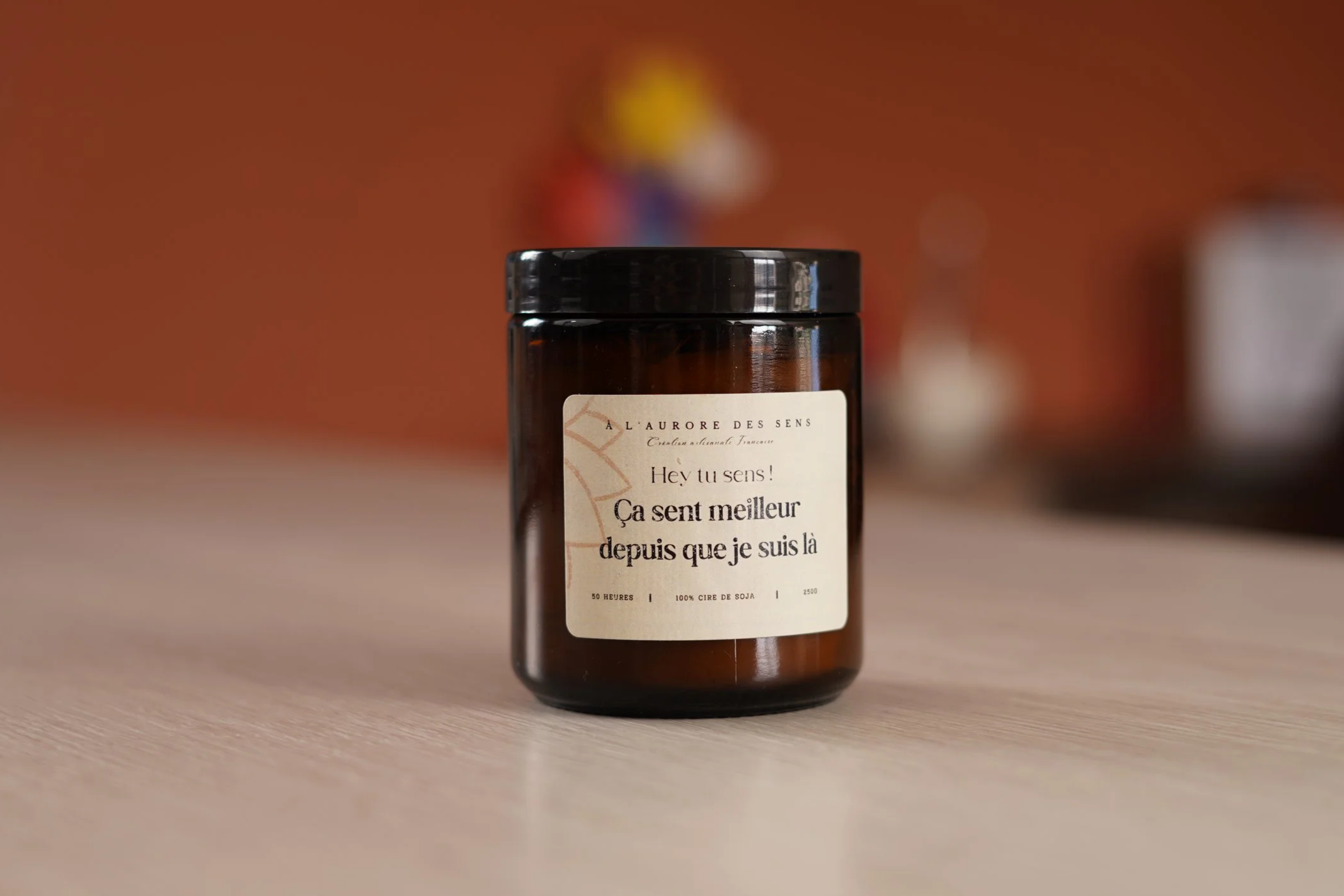 Un pot en verre marron foncé avec un étiquette blanche indiquant qu'il s'agit d'une cire de soja, avec des inscriptions en français.