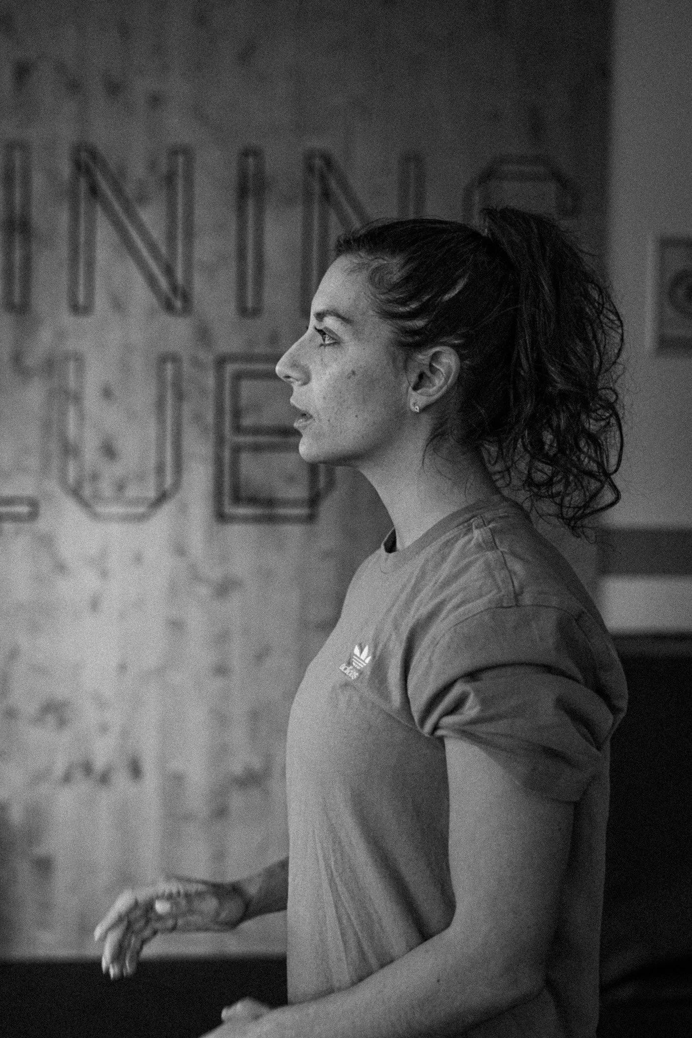 Une femme en profil, portant un t-shirt Adidas, en train de faire un mouvement avec ses bras dans une salle d'entraînement.
