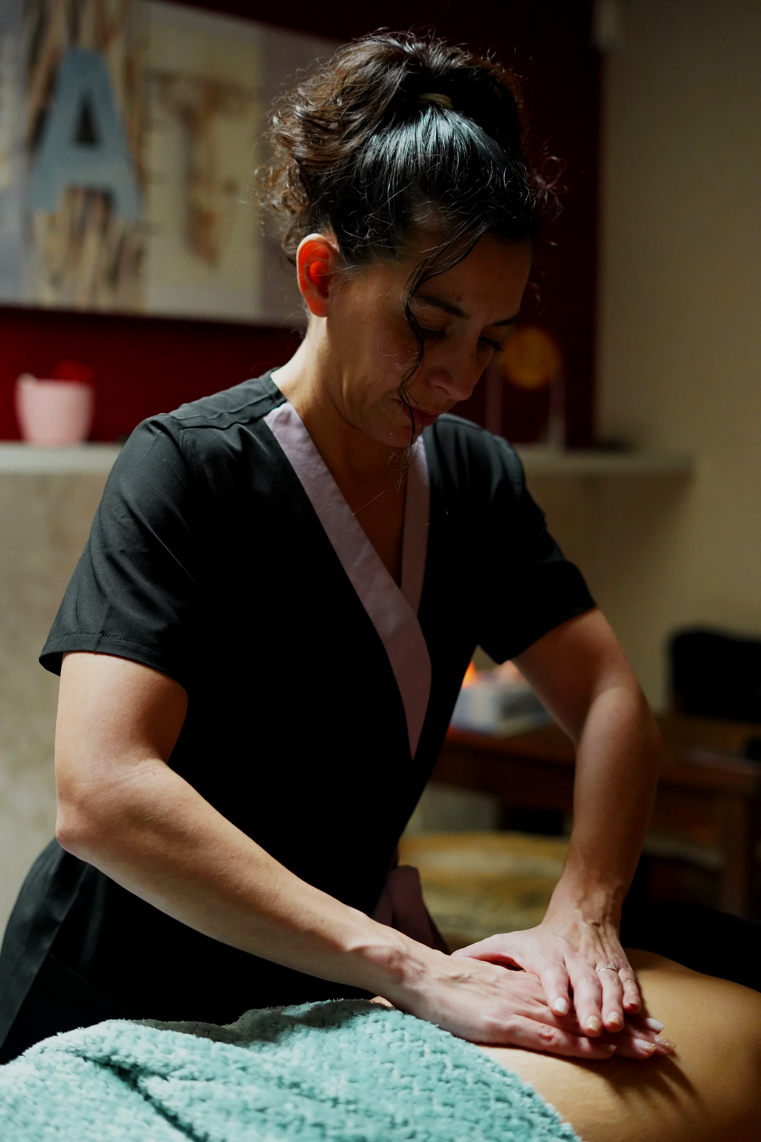 Une femme effectue un massage sur une personne allongée, dans un cadre intérieur chaleureux.
