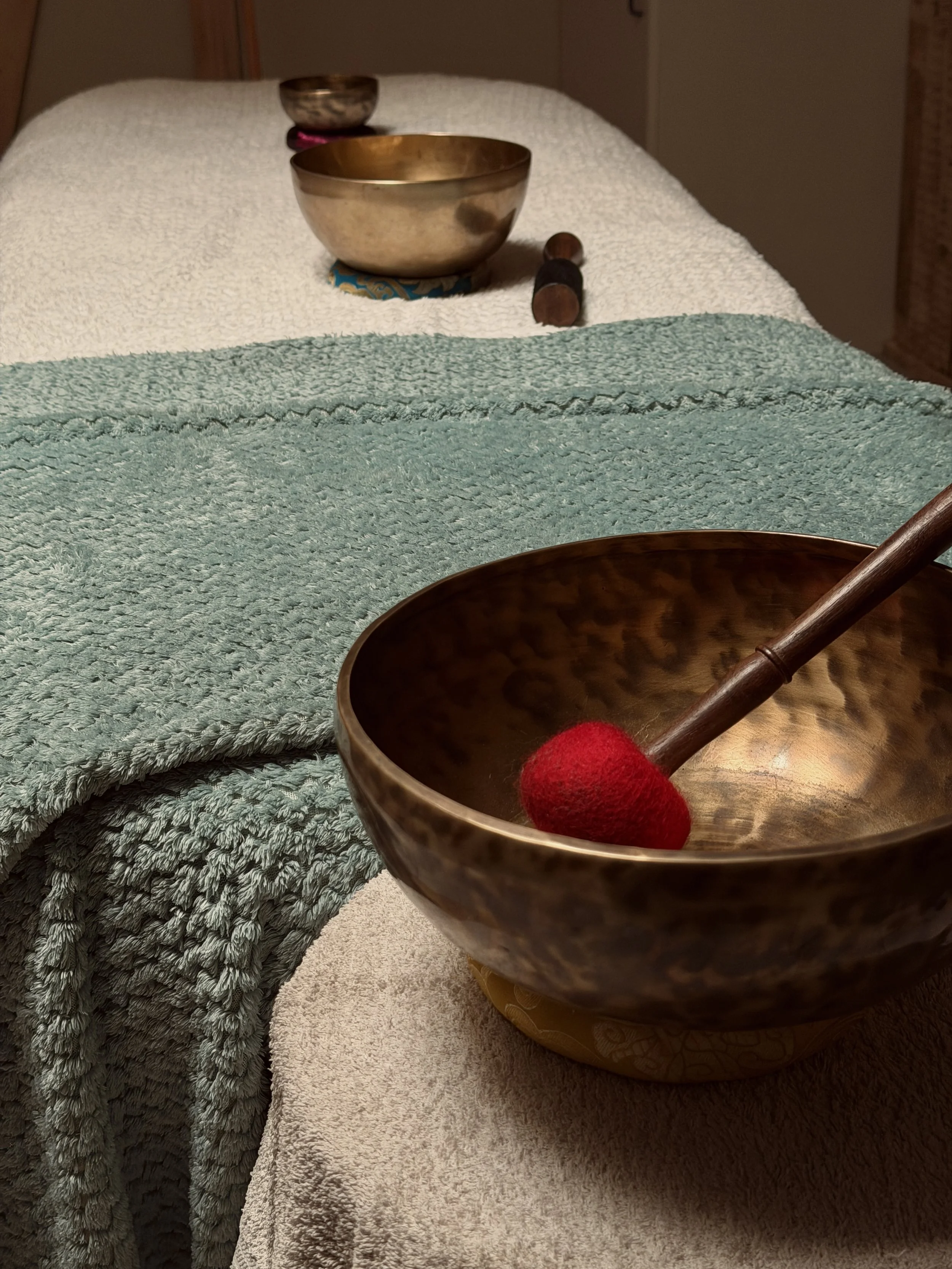Une pièce sonore en forme de bol en bois avec un bâton en bois, dans un environnement de spa ou de massage, avec des serviettes sur une table.