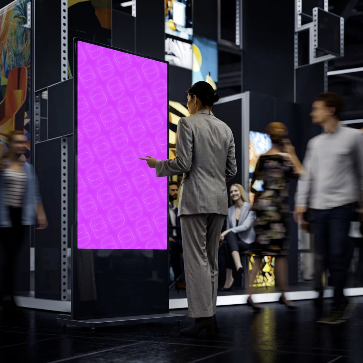 Donna in abito grigio guarda uno schermo digitale grande con sfondo rosa e motivi geometrici, in un ambiente moderno e affollato.