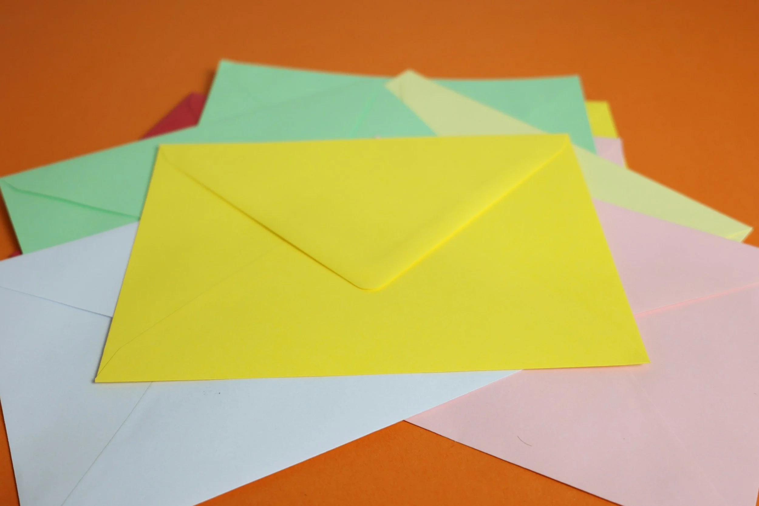 Feuilles de papier de différentes couleurs empilées, visibles en premier plan, avec un fond orange.