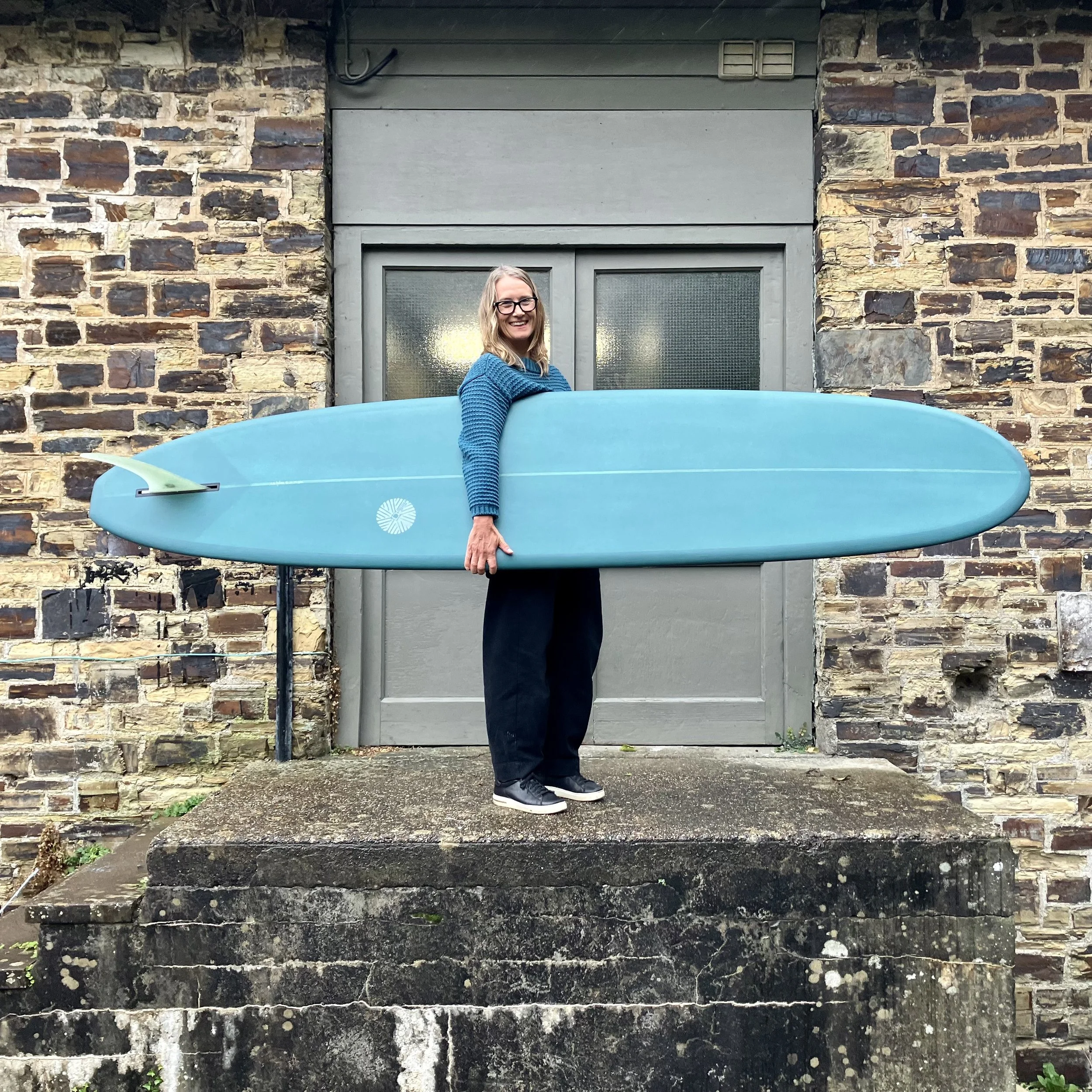 A woman standing on a concrete block holding a surfboard.