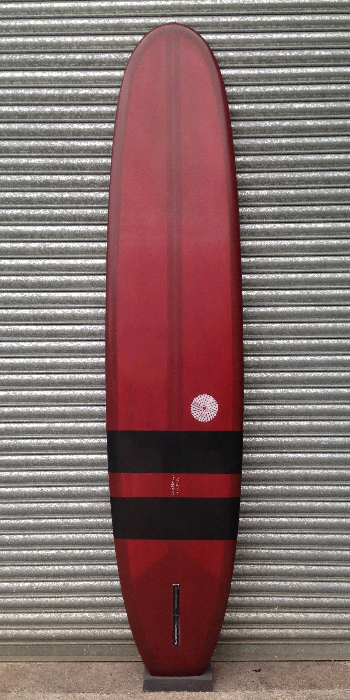Red surfboard with black stripes leaning against a metal roll-up door.