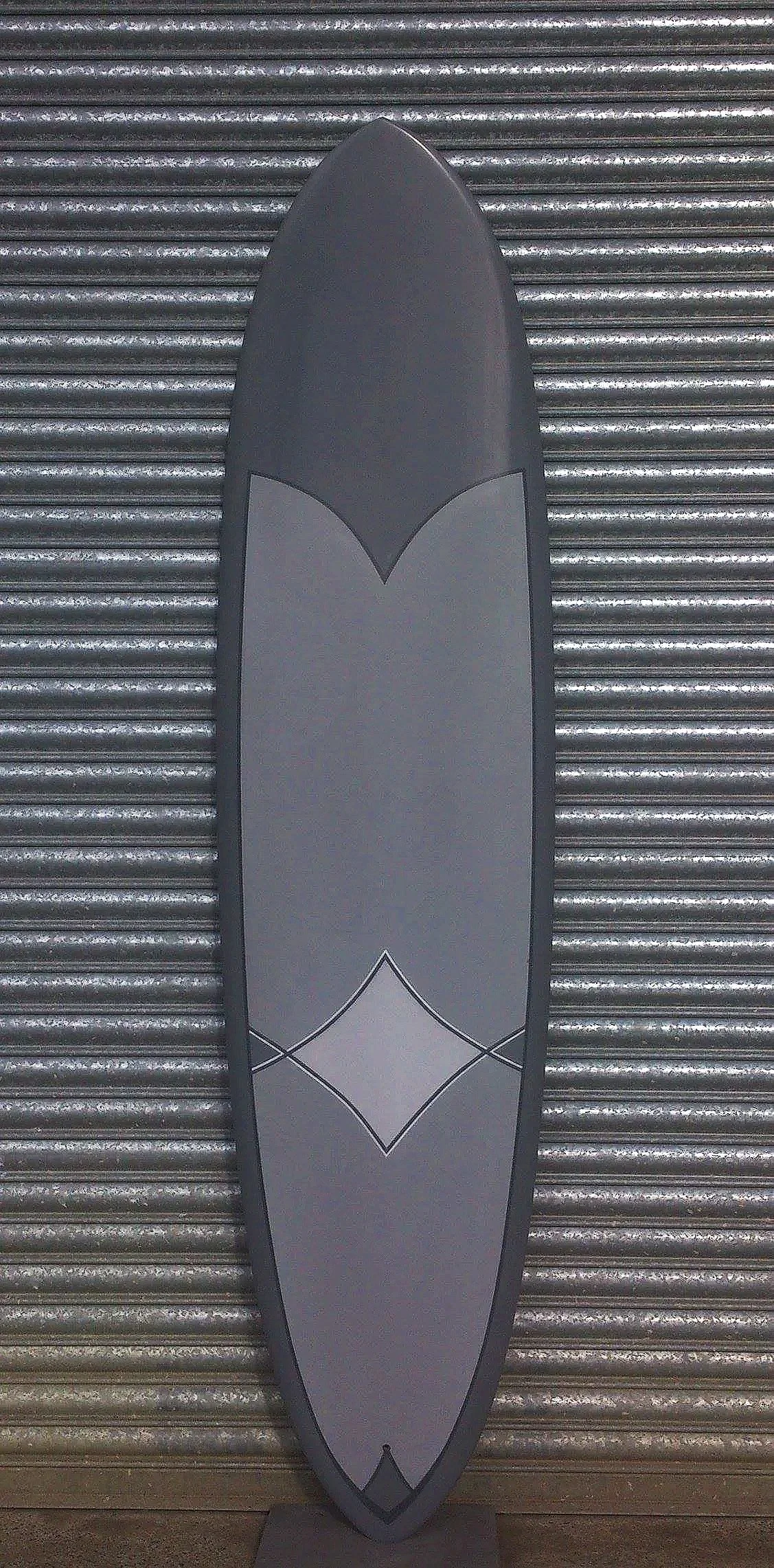 A gray and black stand-up paddleboard with a diamond-shaped design in the center, leaning against a metal garage door.