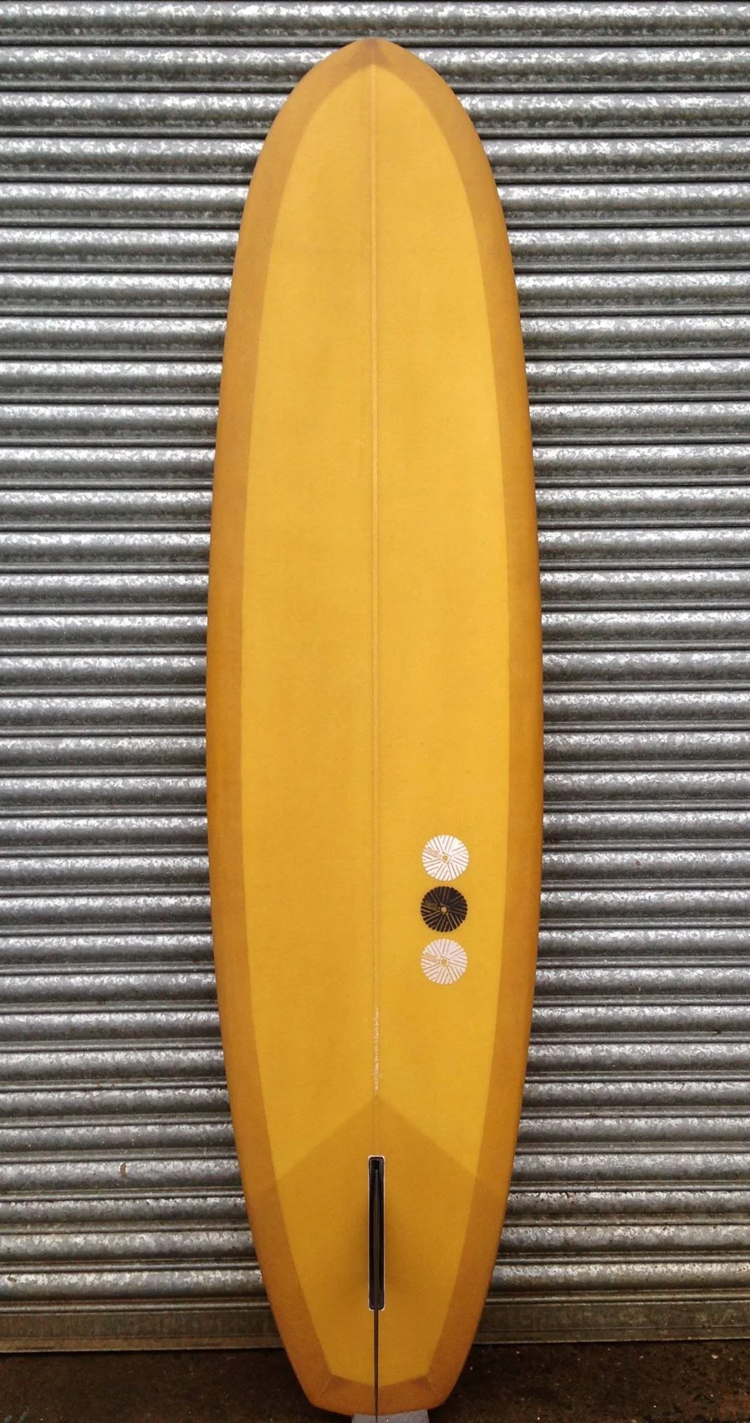 Yellow surfboard standing upright in front of a metal roller shutter door.