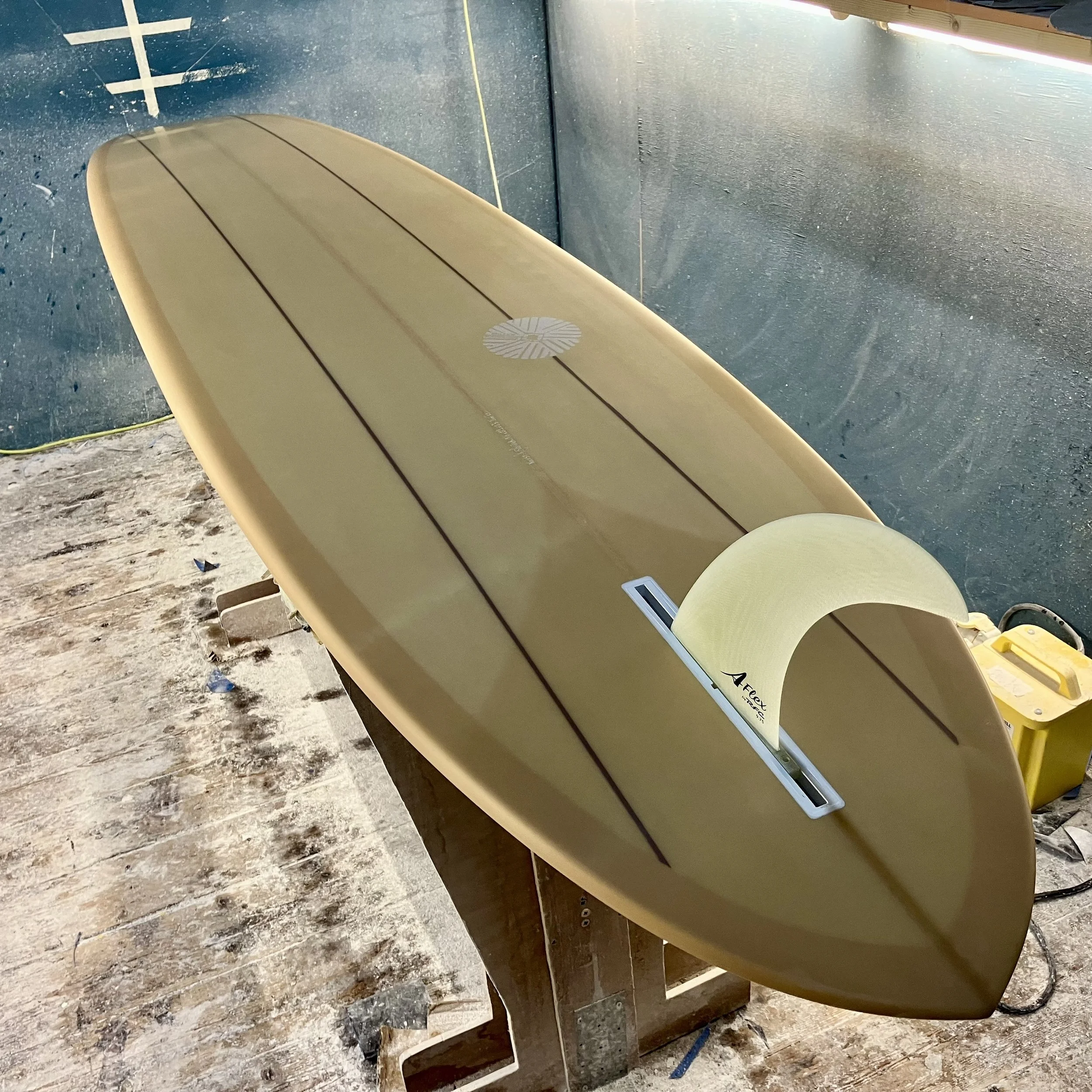 A cream-colored surfboard with dark stripes, placed on a stand in a workshop.