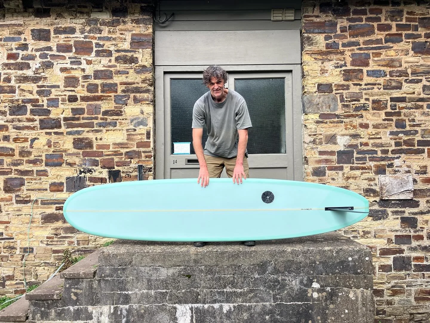 man standing holding a longboard surfboard smiling at the camera