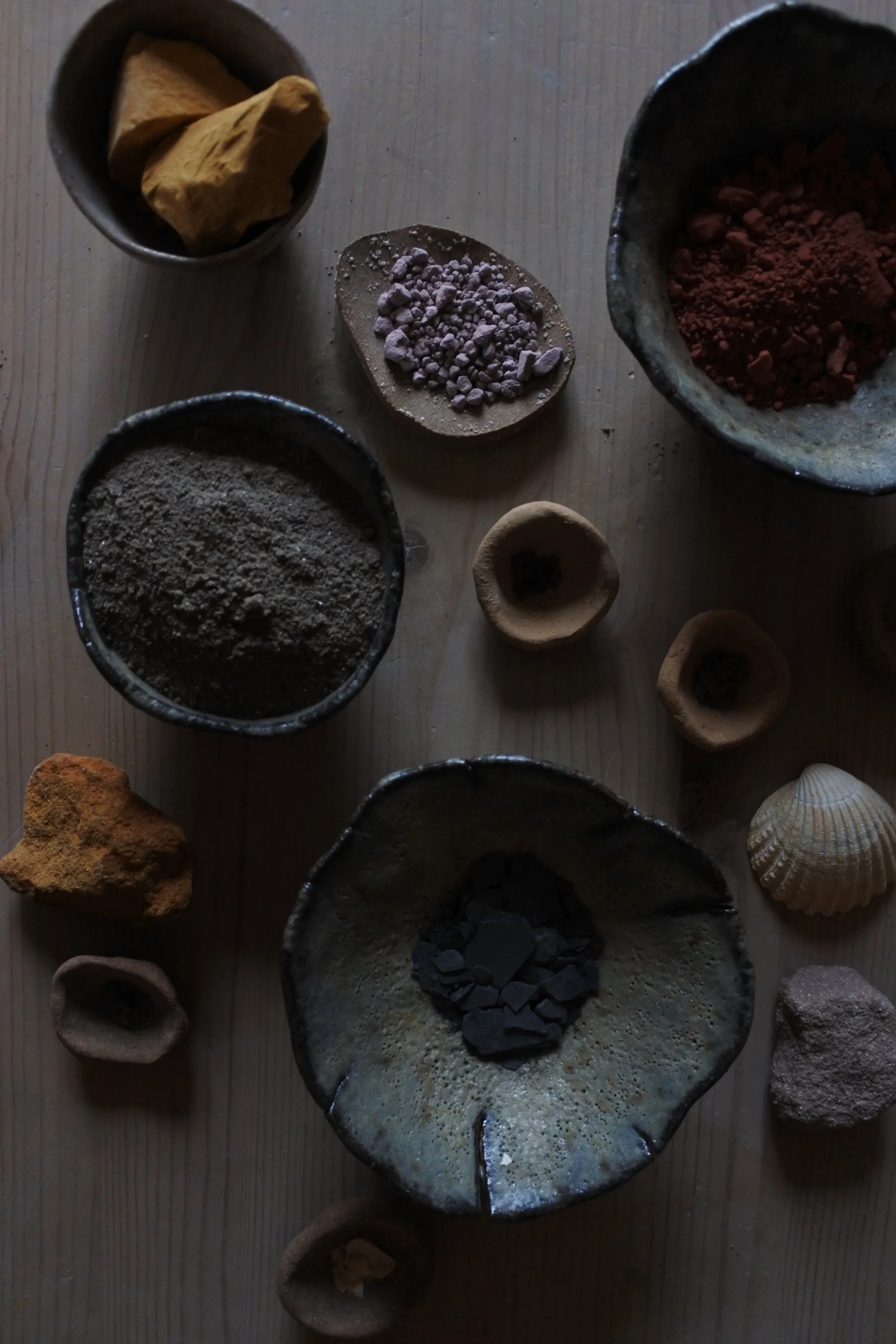 Différentes pierres, poudres et coquillages disposés sur une surface en bois, utilisés pour la fabrication de pigments ou d'ornements.