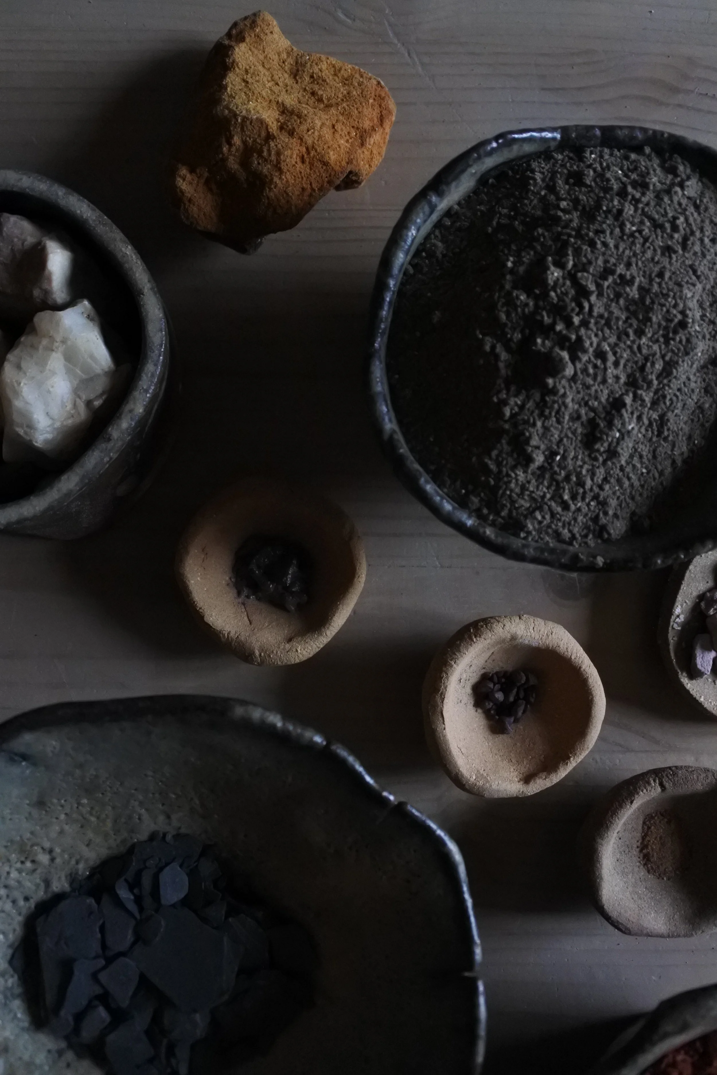 Différents types de cendres, de charbon, de pierre et de matériaux minéraux dans des bols en céramique sur une surface en bois.