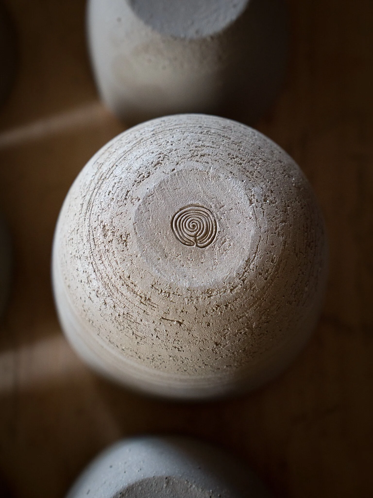 Vue du dessous d'une sculpture en forme de boule en argile, avec un motif en spirale au centre. La surface est texturée avec des lignes concentriques.