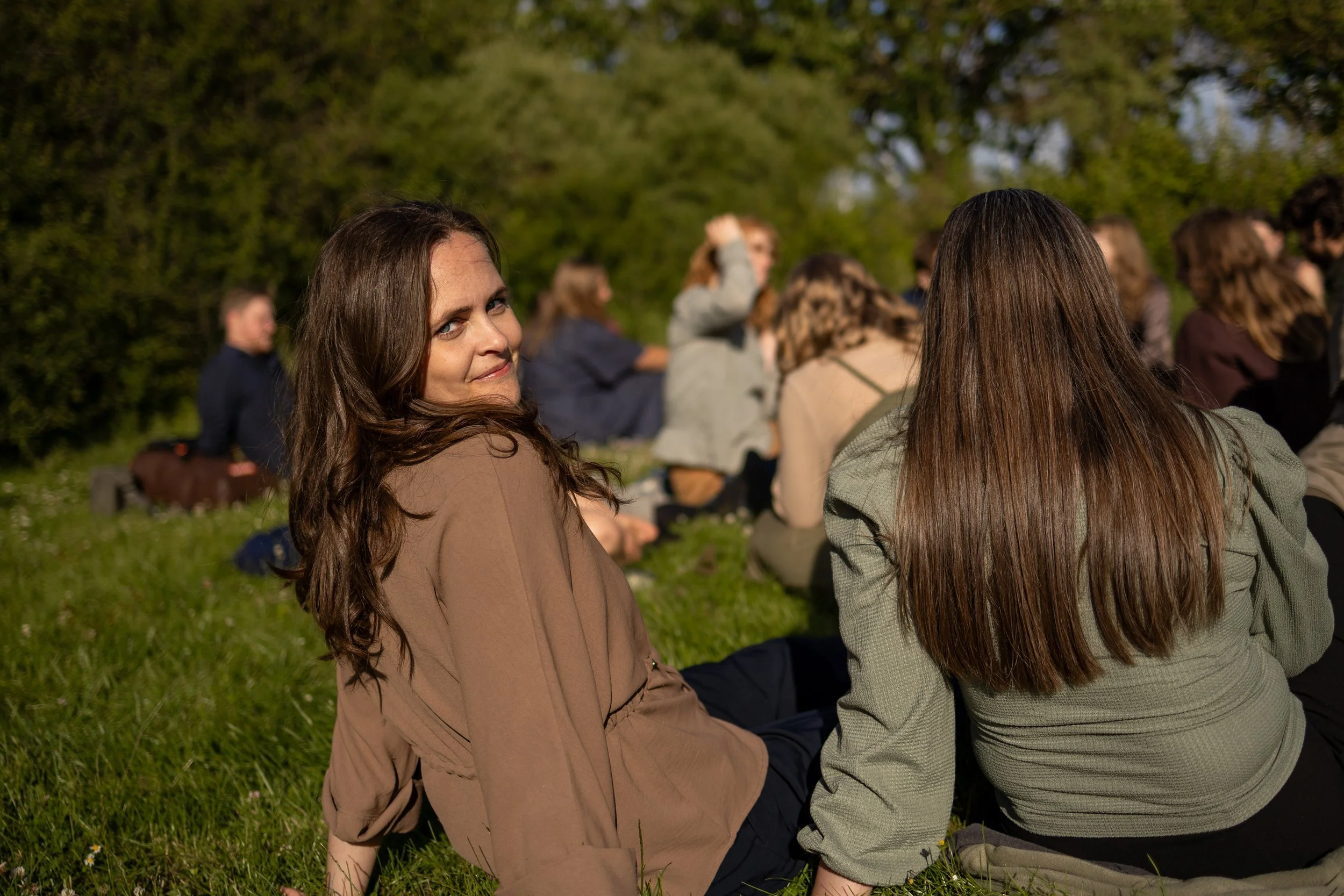People sitting on grass outdoors during daytime, with trees in the background.