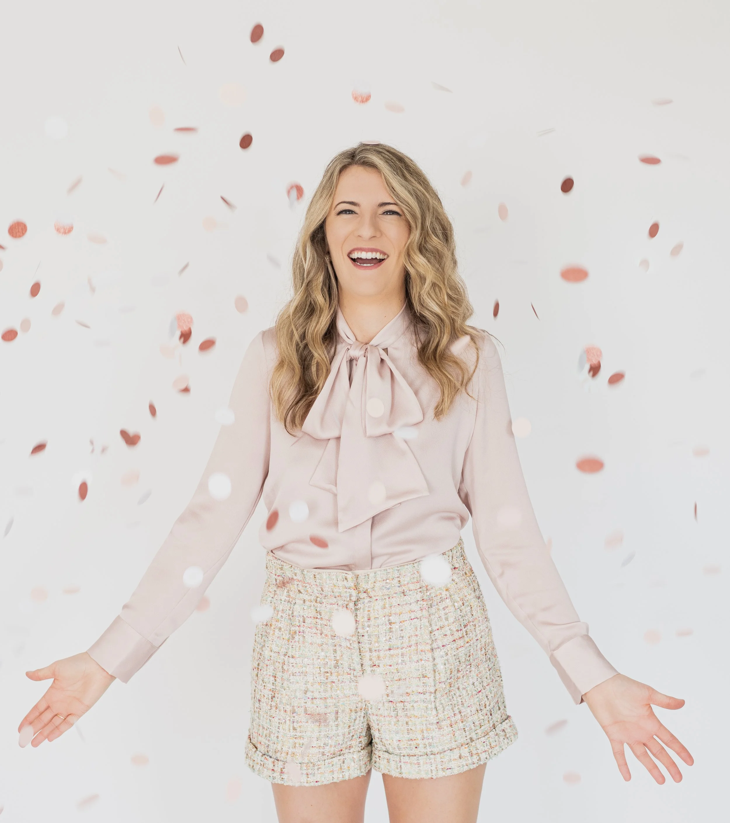 A woman celebrating with confetti falling around her, smiling with open arms.