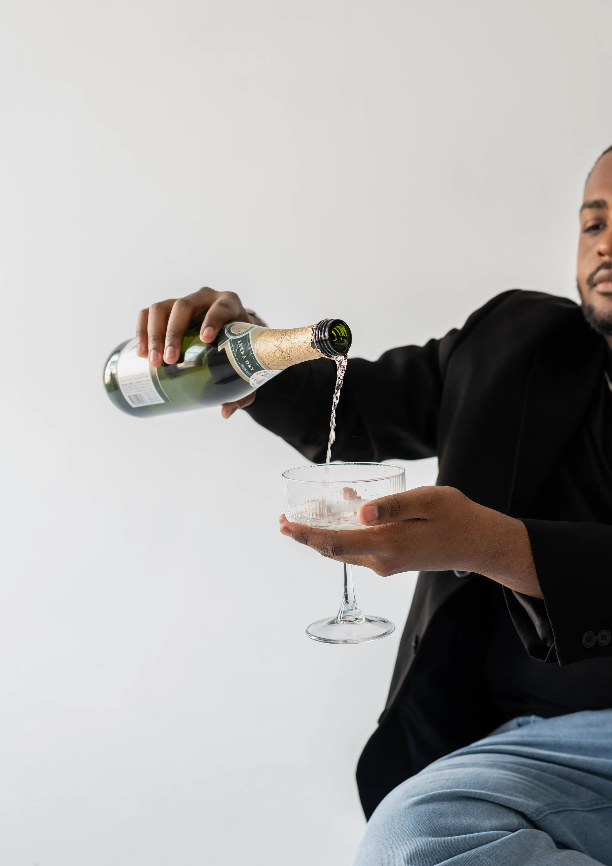 A man in a black blazer pouring champagne into a cocktail glass.