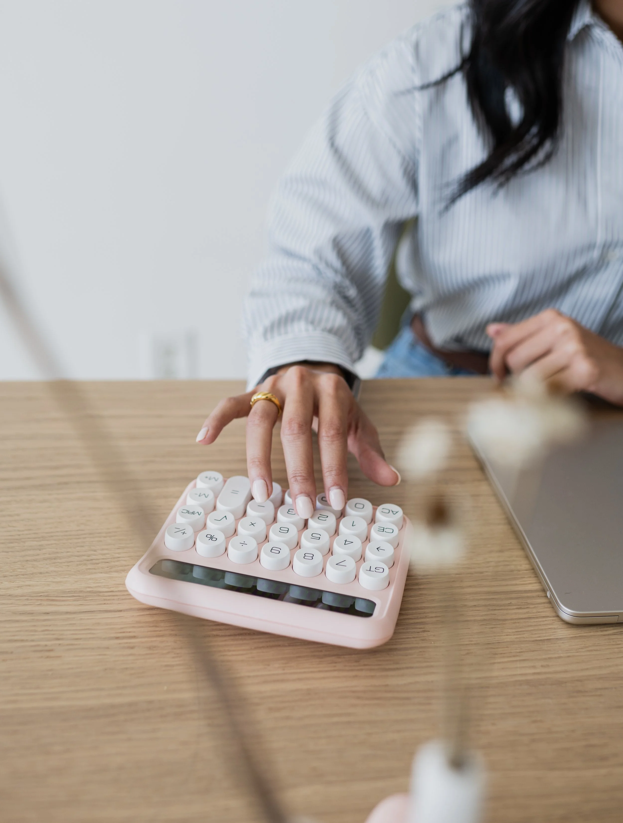 Person using a pink calculator at a wooden desk with a laptop nearby.