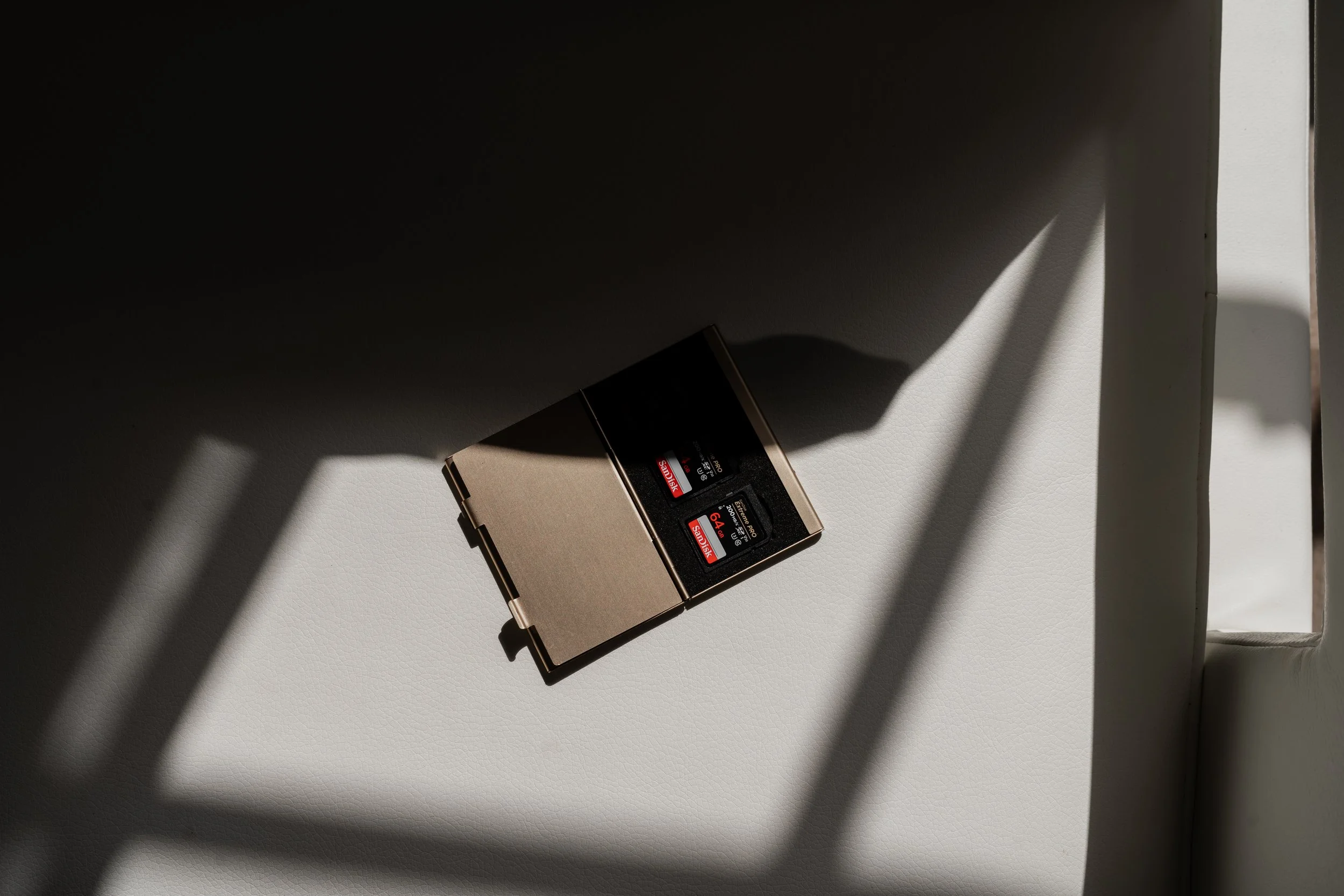 A 64GB black SD card in a beige plastic case sitting on a light-colored surface with shadows cast from nearby window blinds.