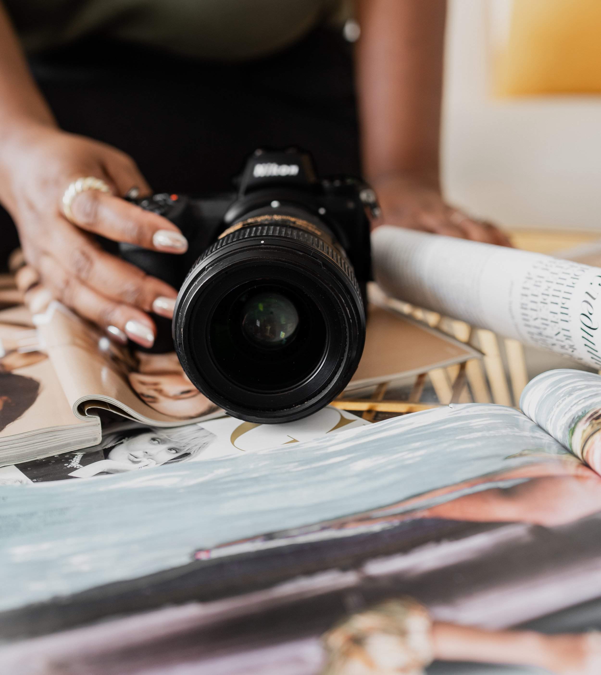 Close-up of a camera on top of fashion magazines, with a woman's hands nearby.