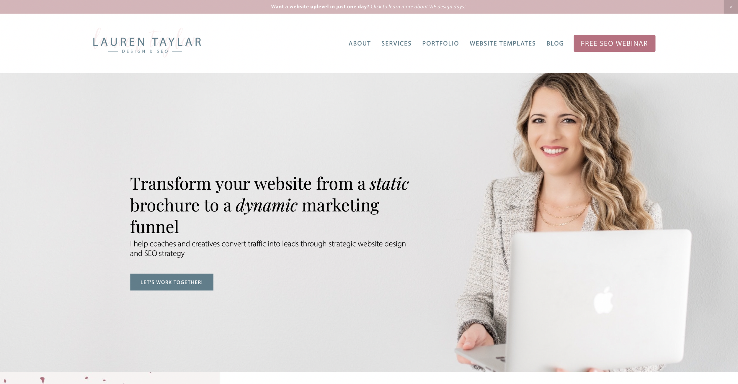 A woman with long blonde curly hair smiling while holding a silver laptop, standing against a light gray wall.