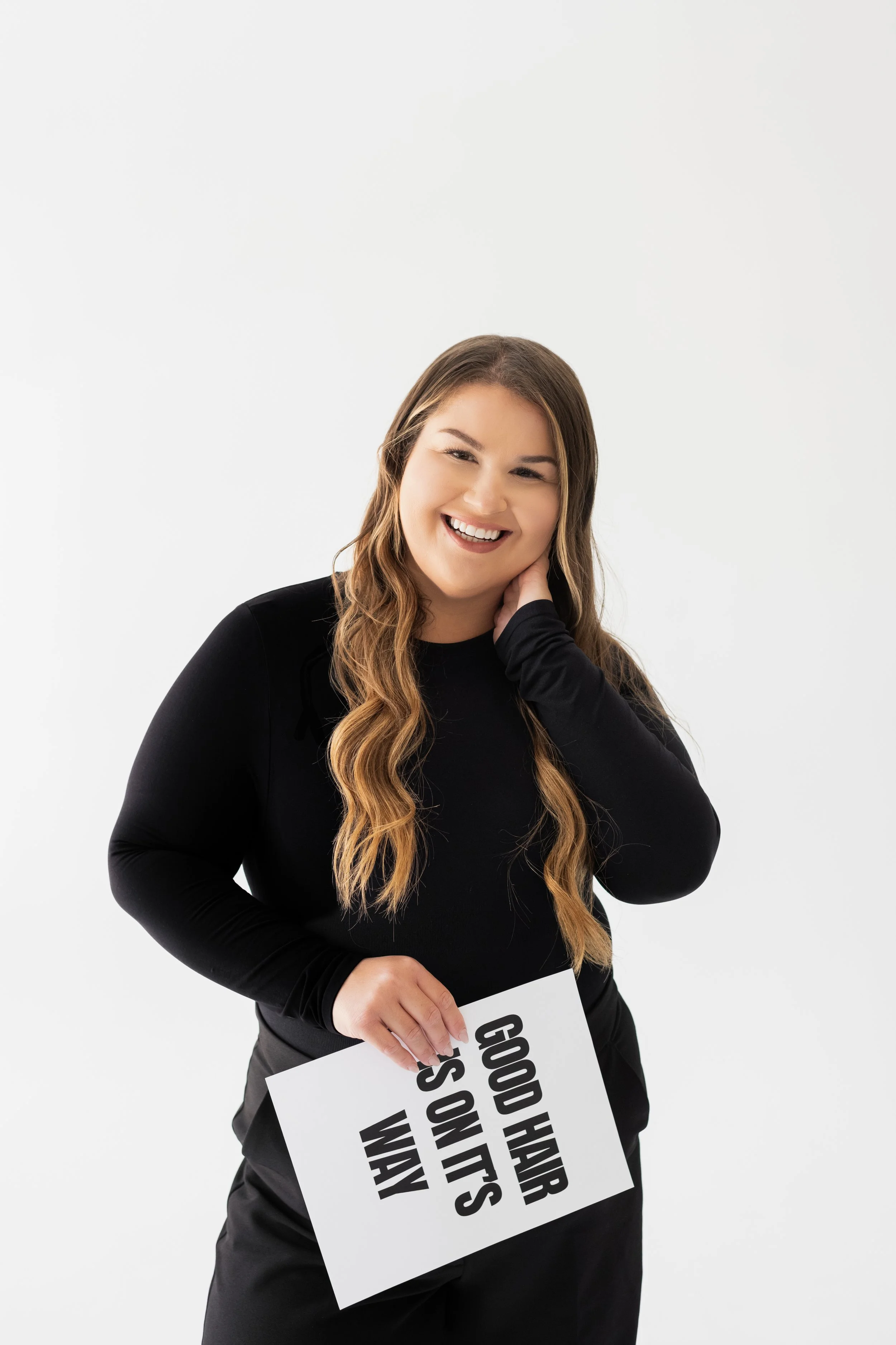A young woman with long wavy hair, smiling and holding a sign that says 'GOD HAR HAS UTS WAM' against a white background.