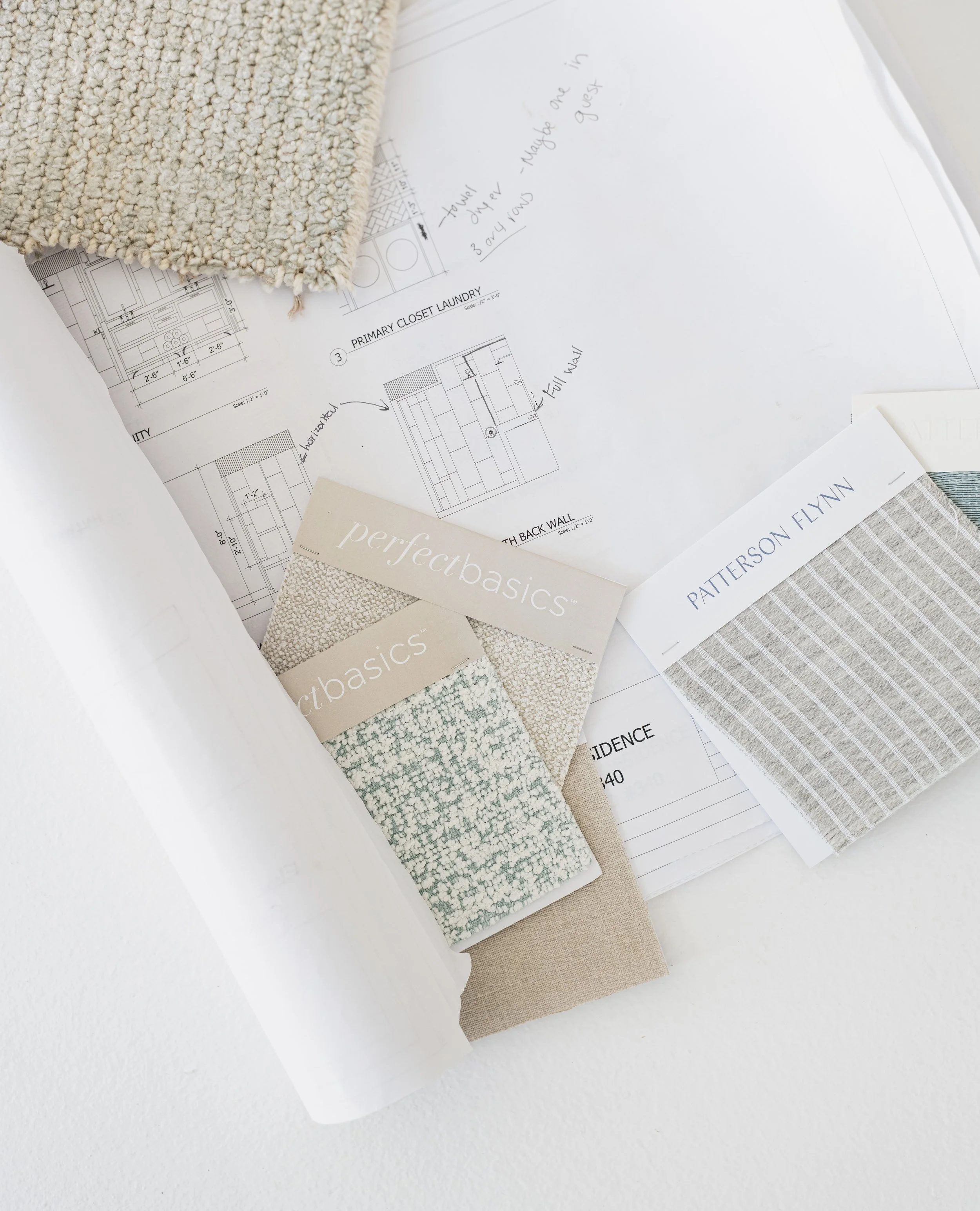 Interior design planning materials including fabric swatches labeled 'perfect basics' and 'pattern Flynn,' blueprints, and handwritten notes on construction details.