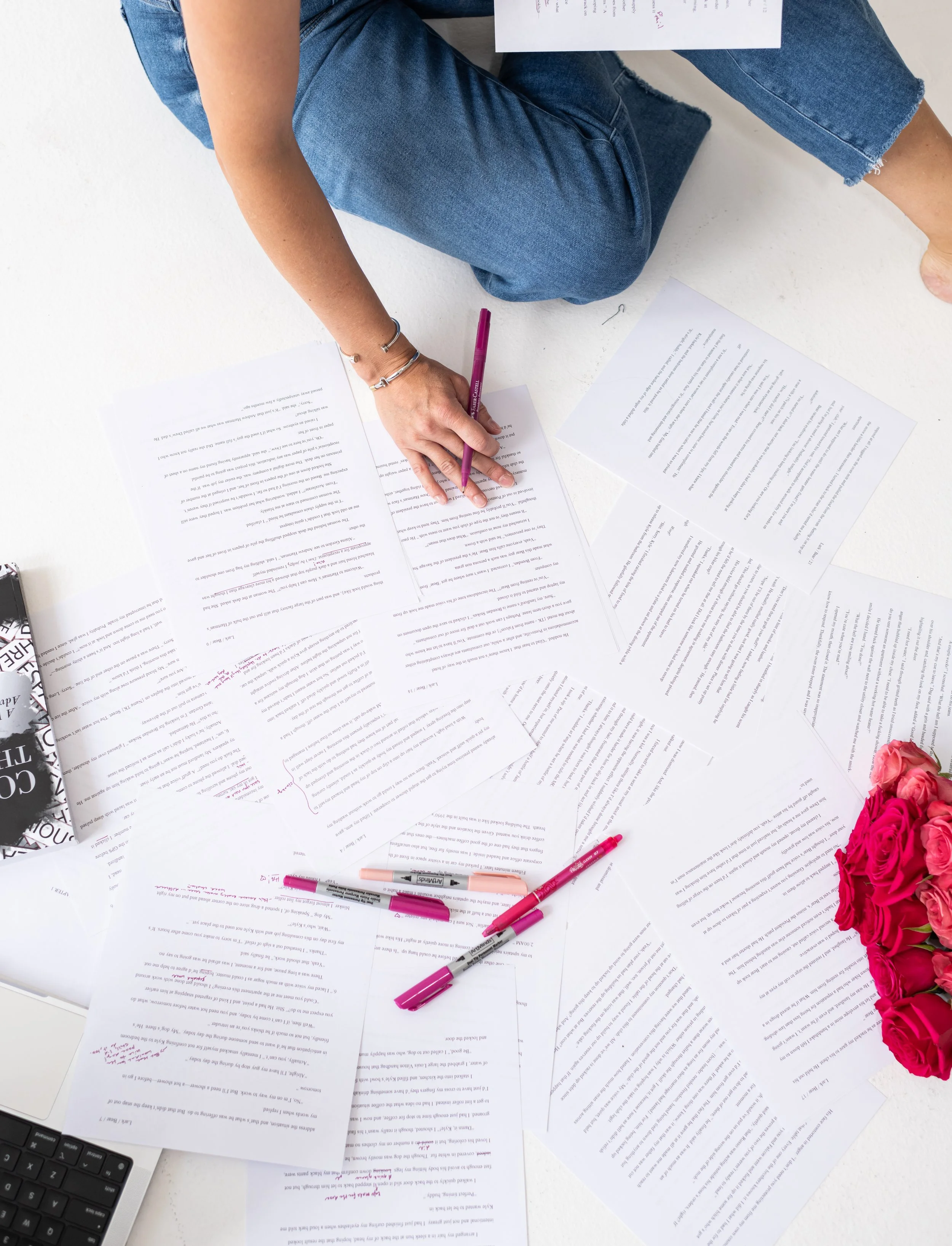 Person sitting on the floor with scattered papers, pens, and flowers, working on documents.