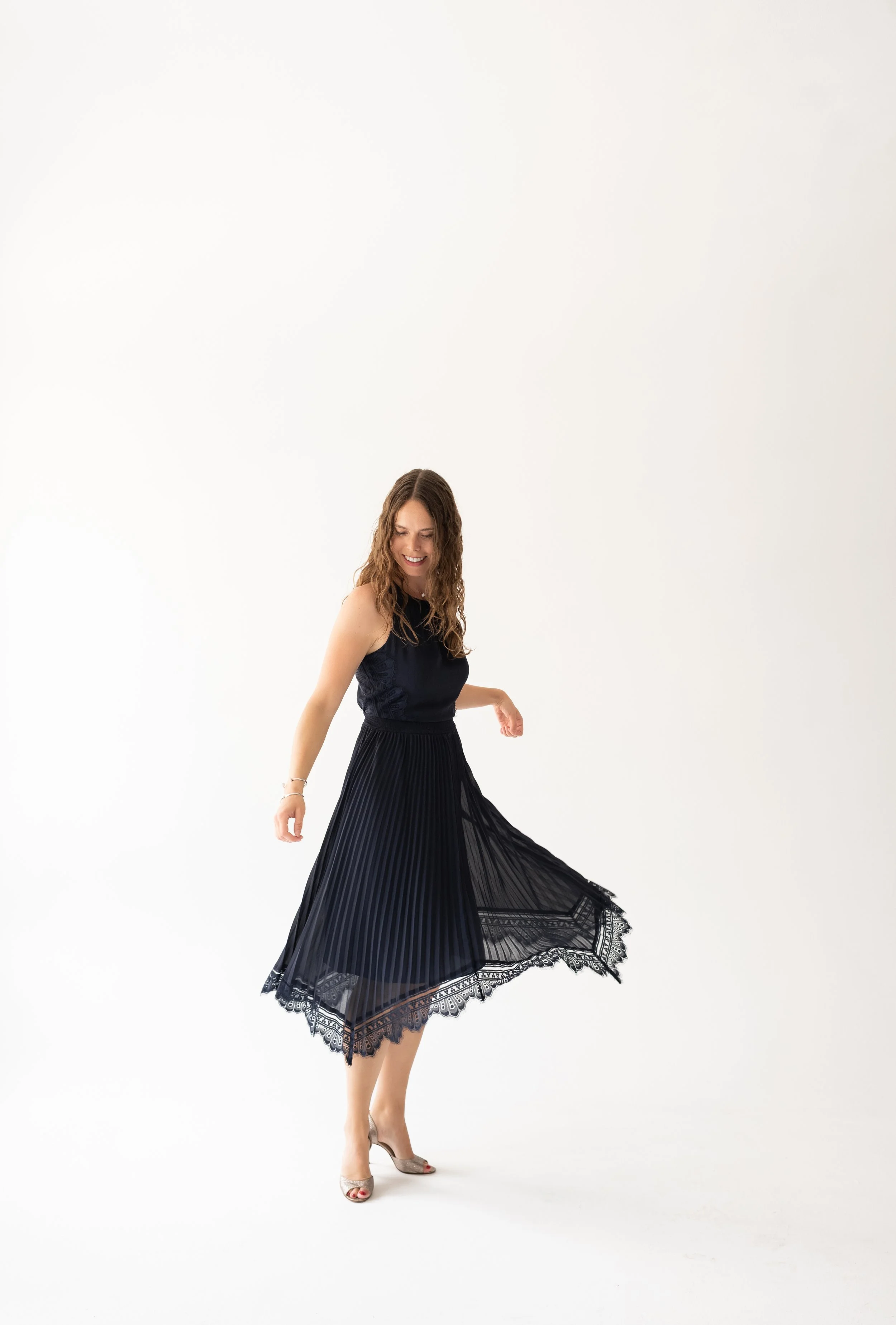 Woman in black dress spinning and smiling on a white background.
