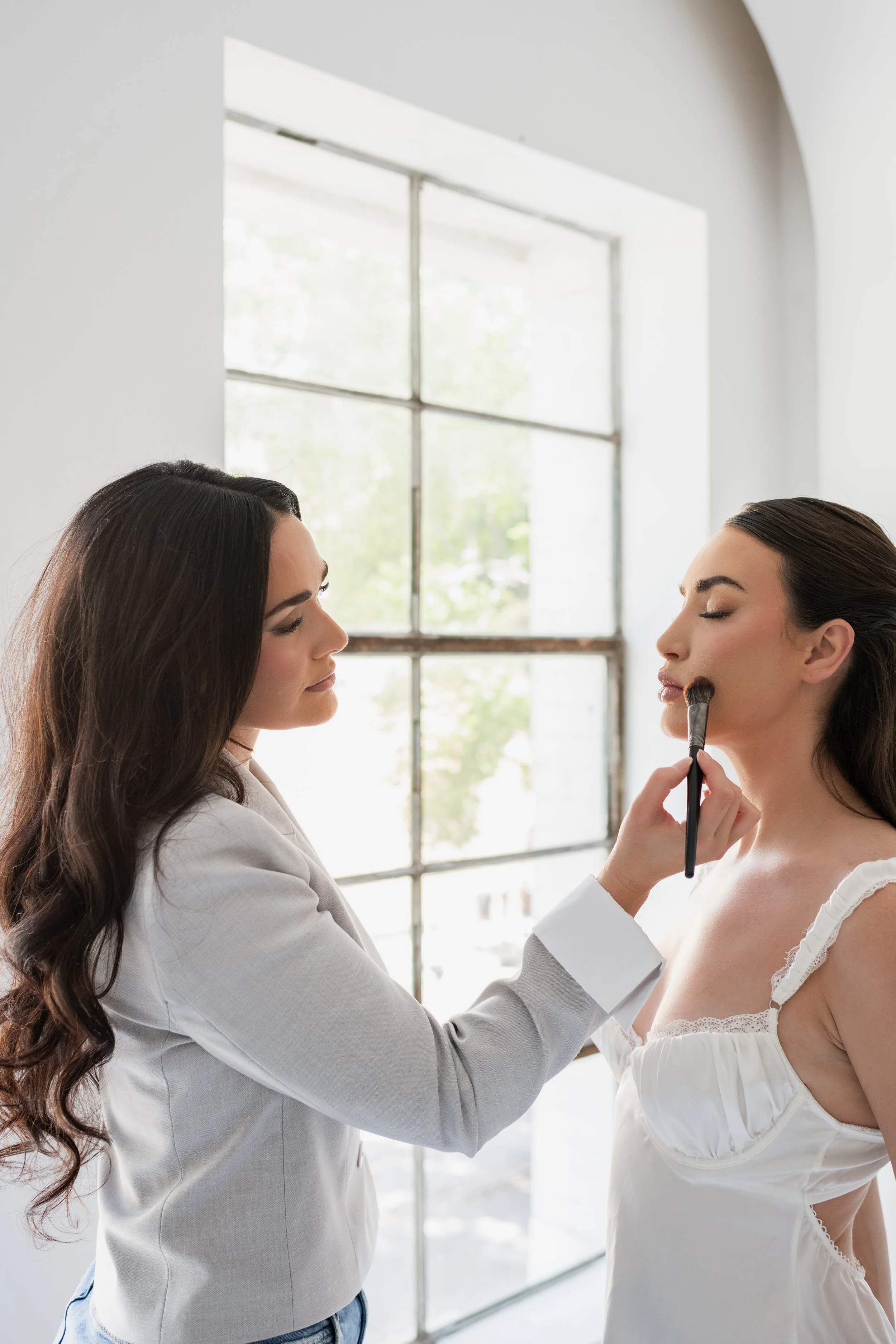 Makeup artist applying makeup to woman near window.
