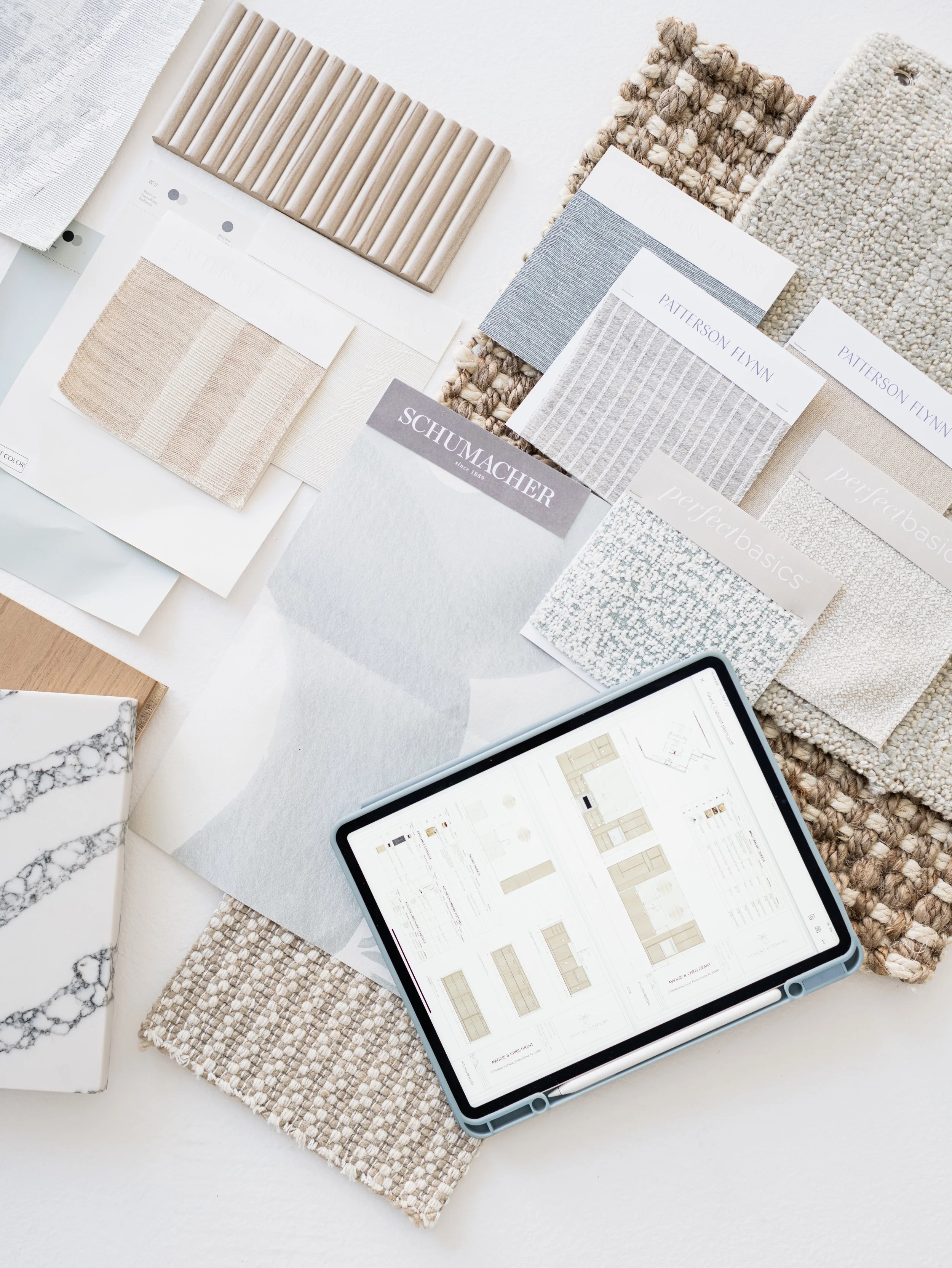 Interior design materials spread including fabric and tile samples, color swatches, an iPad with design plans, and a Schumacher color sample sheet.