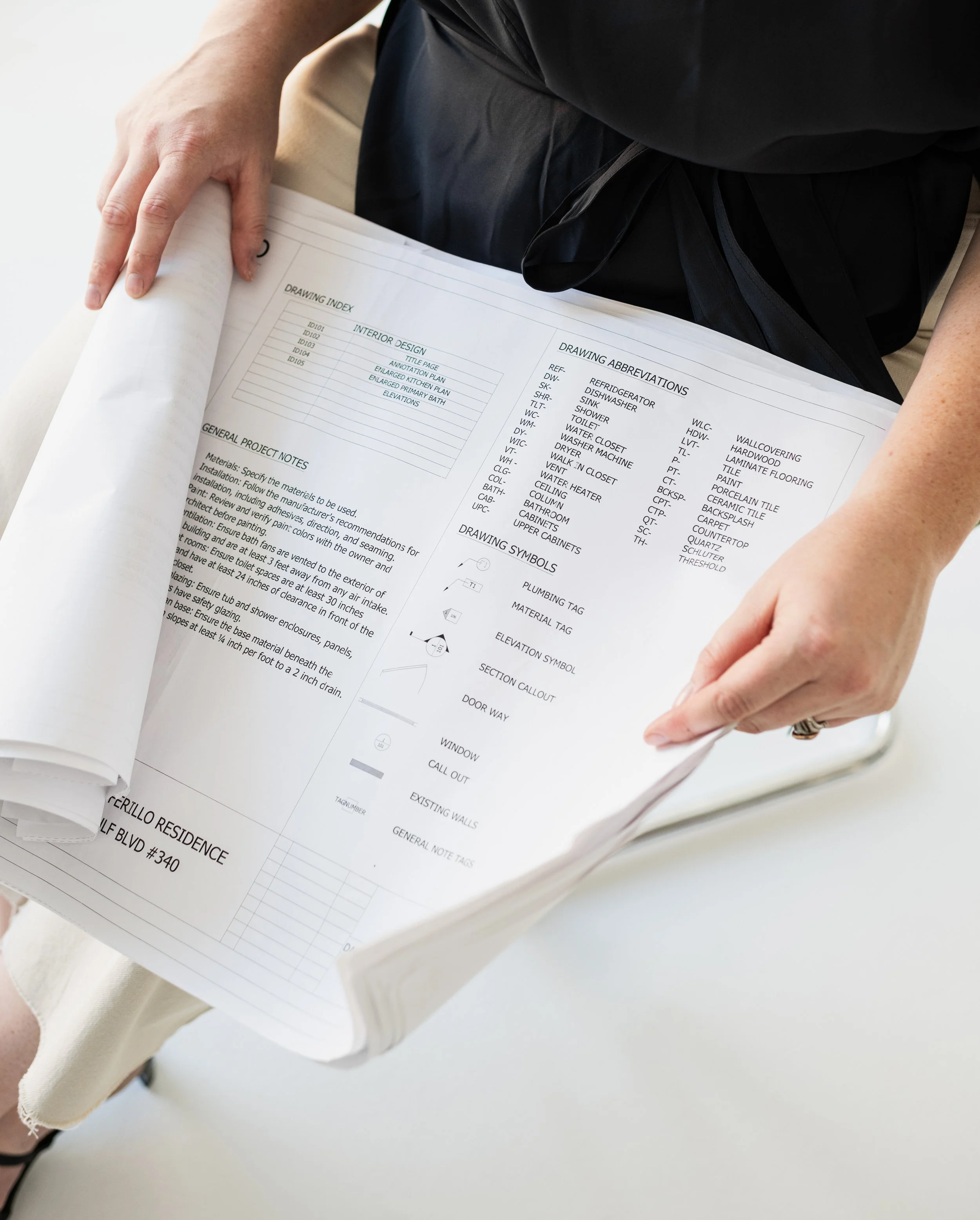 A person holding a large rolled architectural blueprint showing interior design notes and drawing symbols.