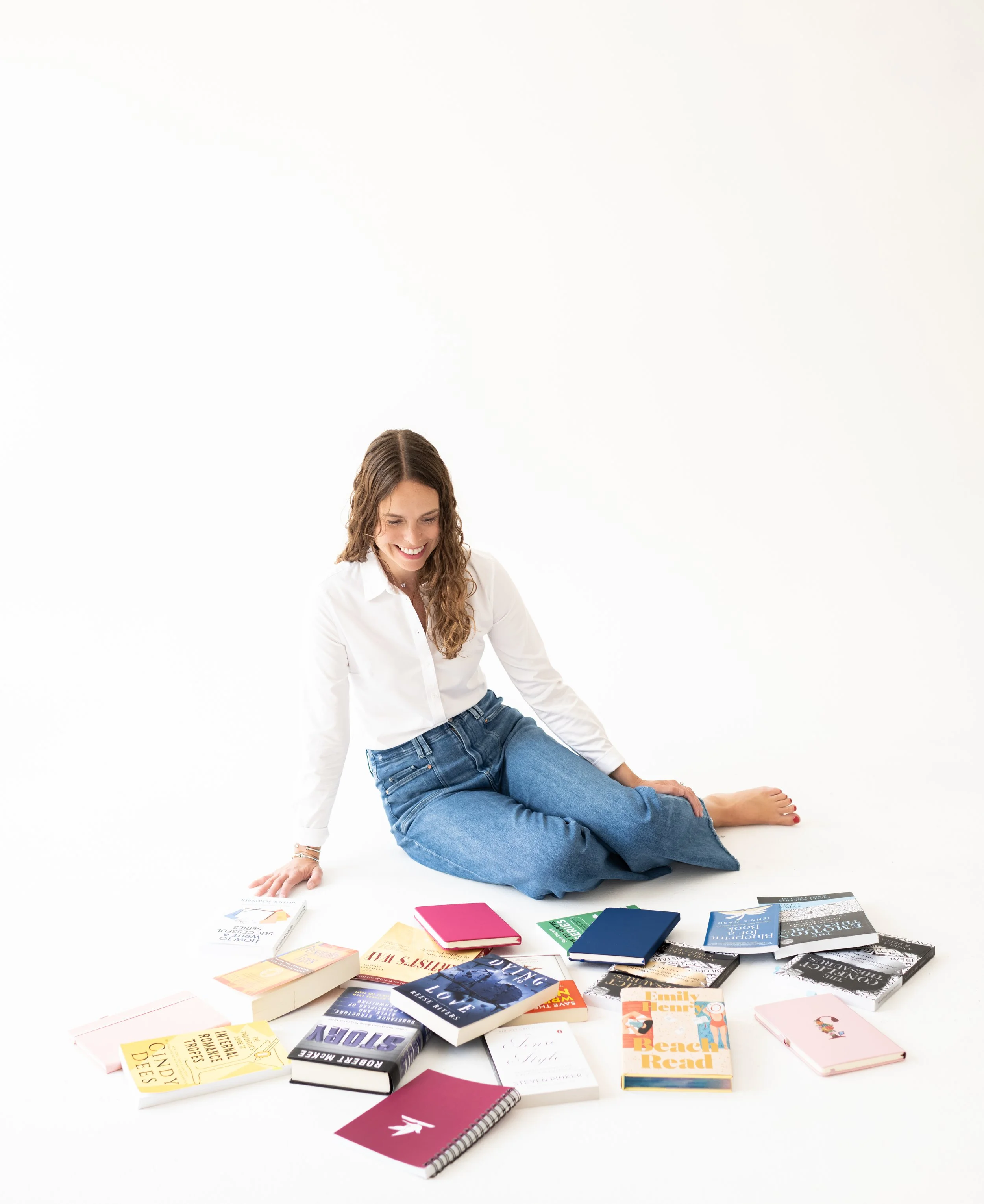 Woman sitting on the floor surrounded by books and notebooks, smiling.