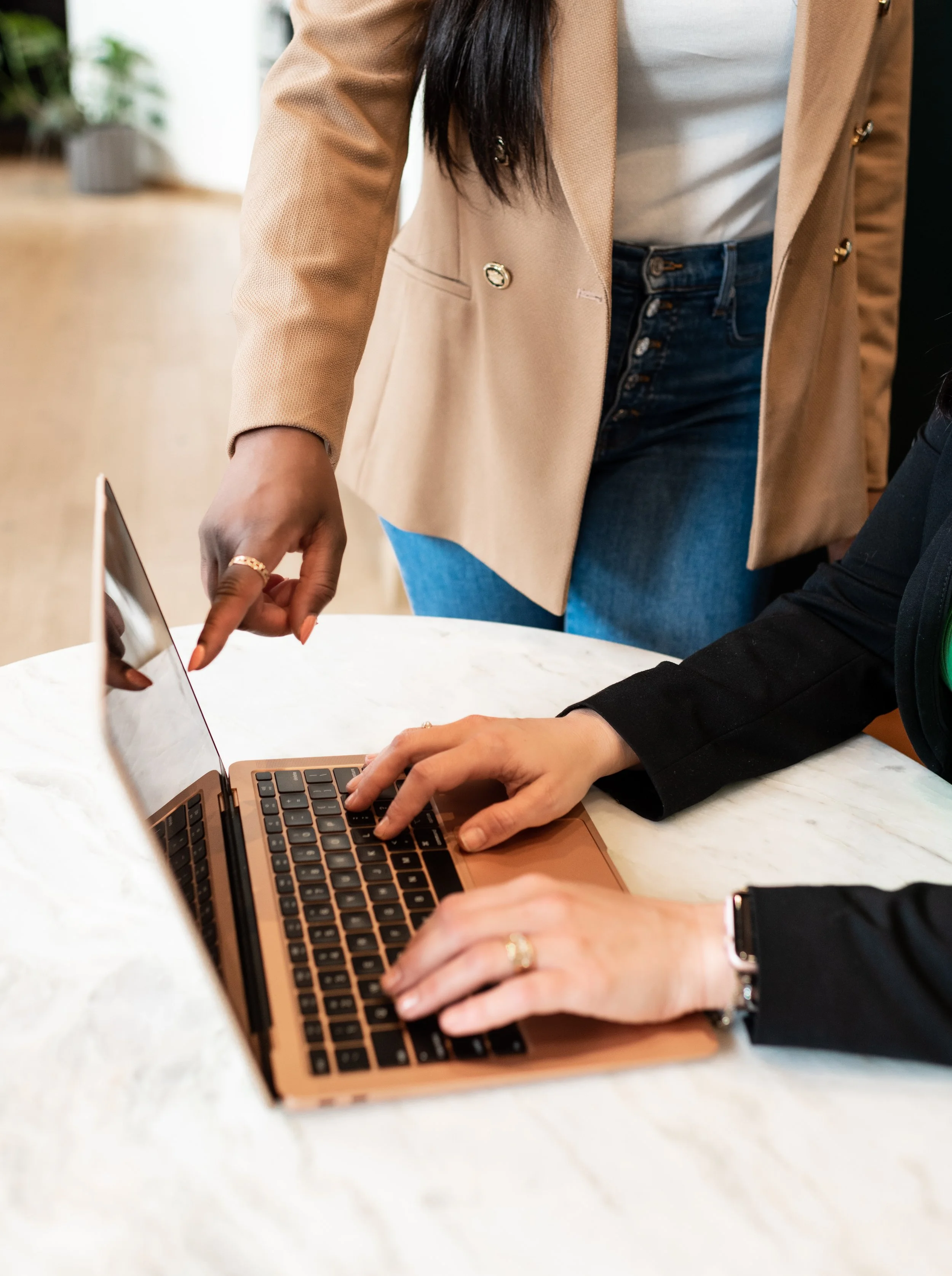 Two people working at a marble table with a laptop and a tablet, one person is pointing at the tablet while the other is typing on the laptop.