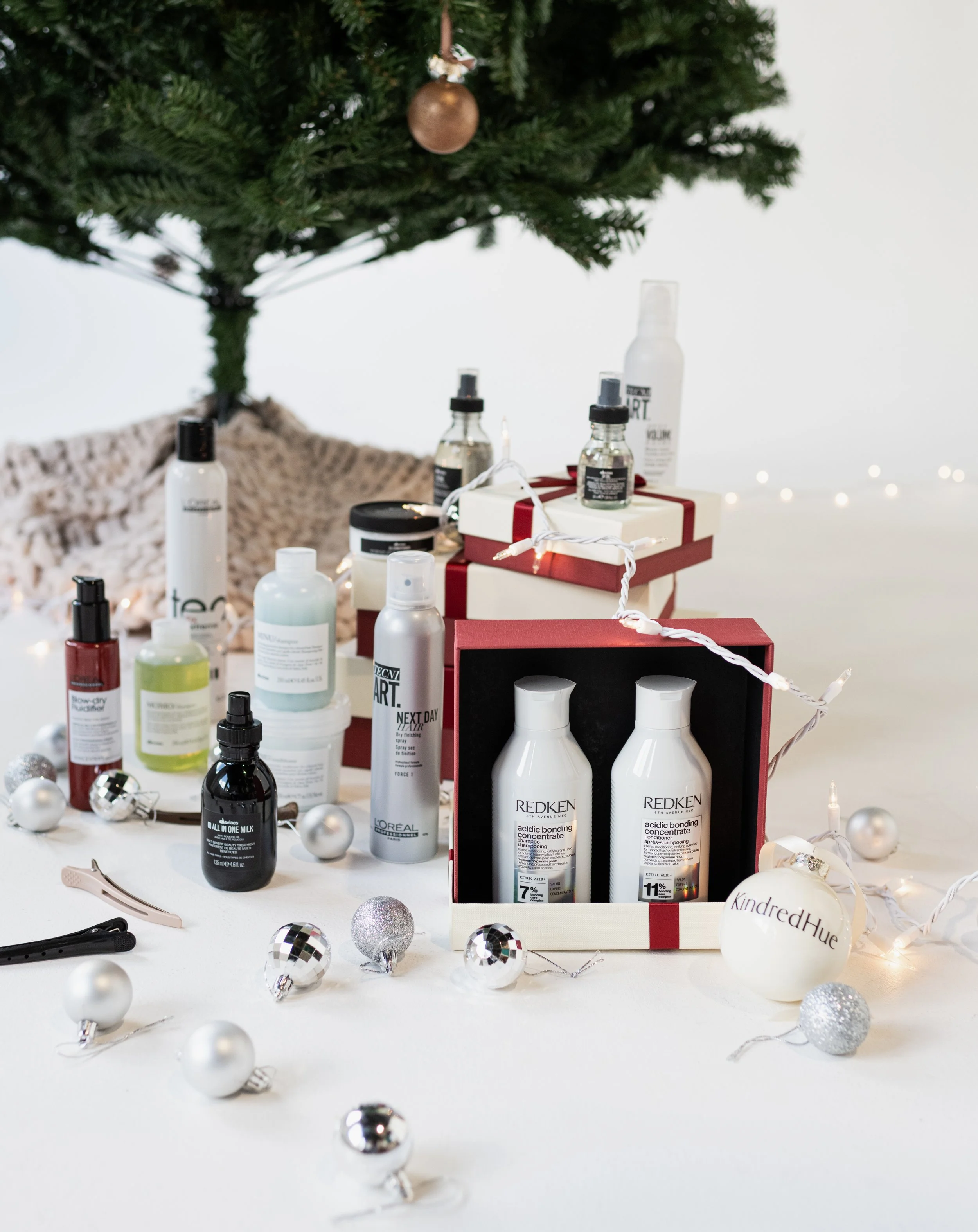 A table decorated with Christmas ornaments and beauty products, with a Christmas tree in the background.
