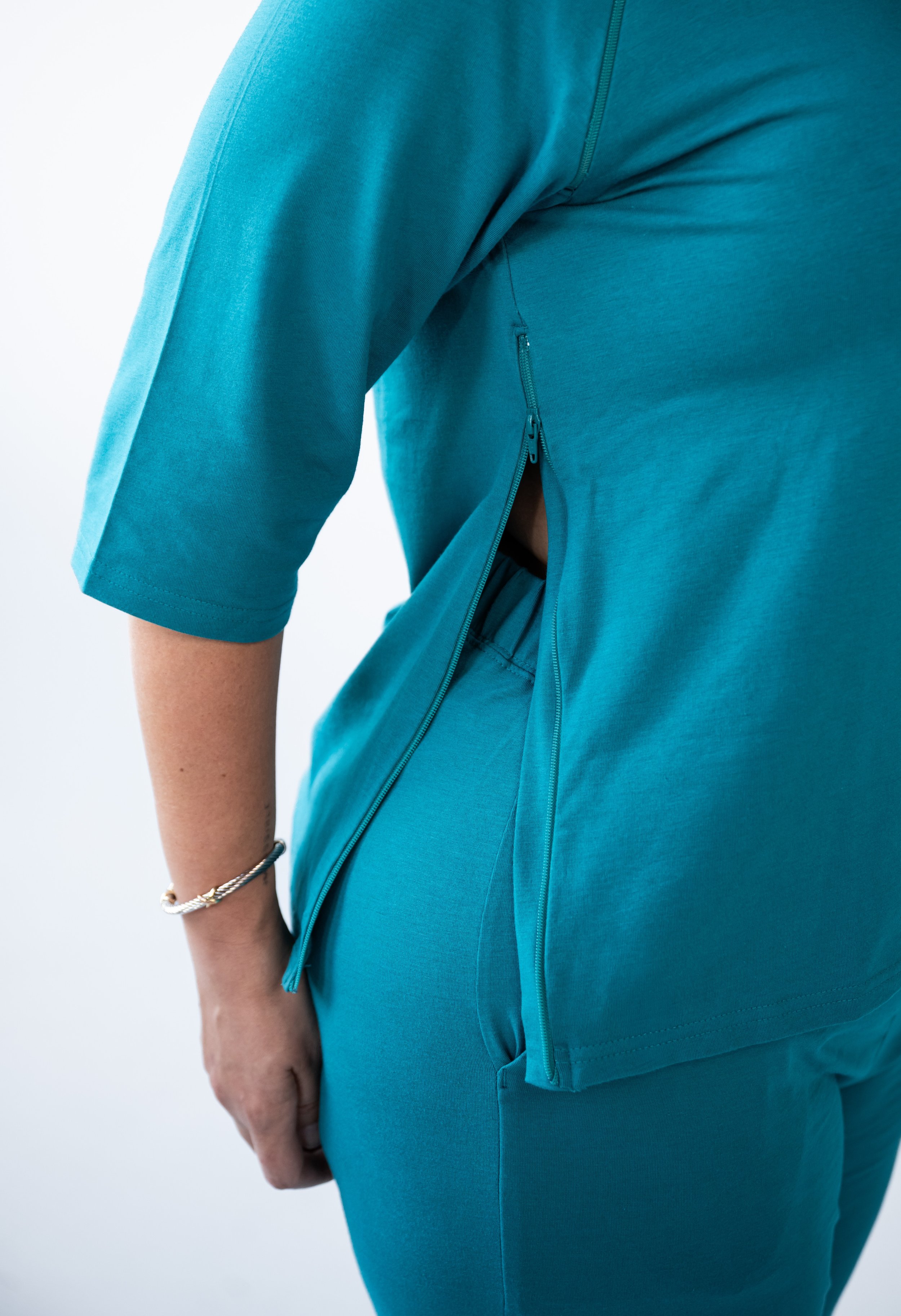 Close-up of a person wearing a teal athletic shirt and matching pants, with a zipper detail on the side of the shirt revealing part of their skin.