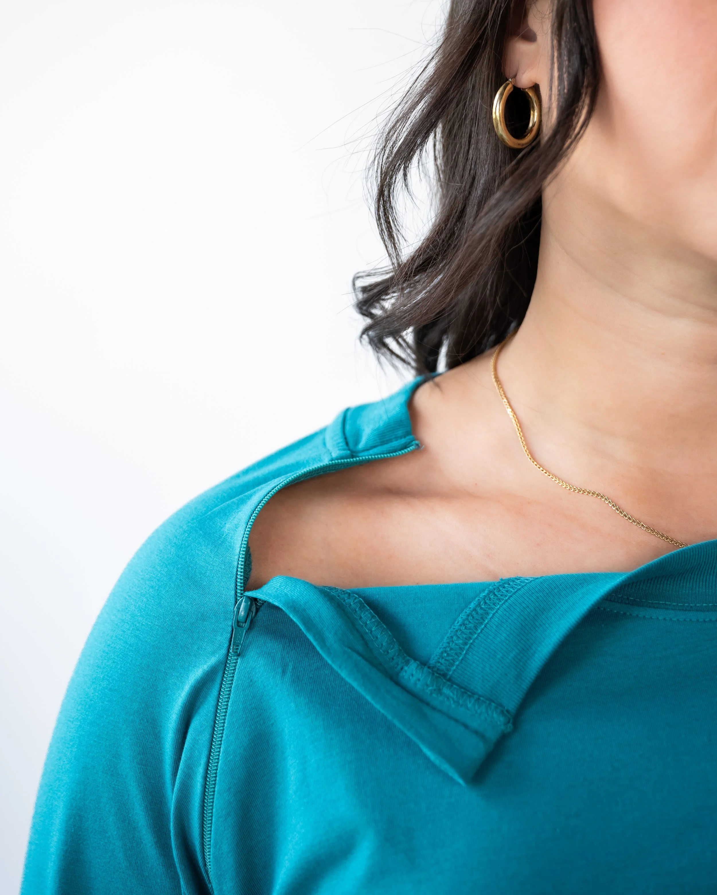 Close-up of a woman wearing a turquoise athletic top with a zipper and a gold necklace and hoop earrings.