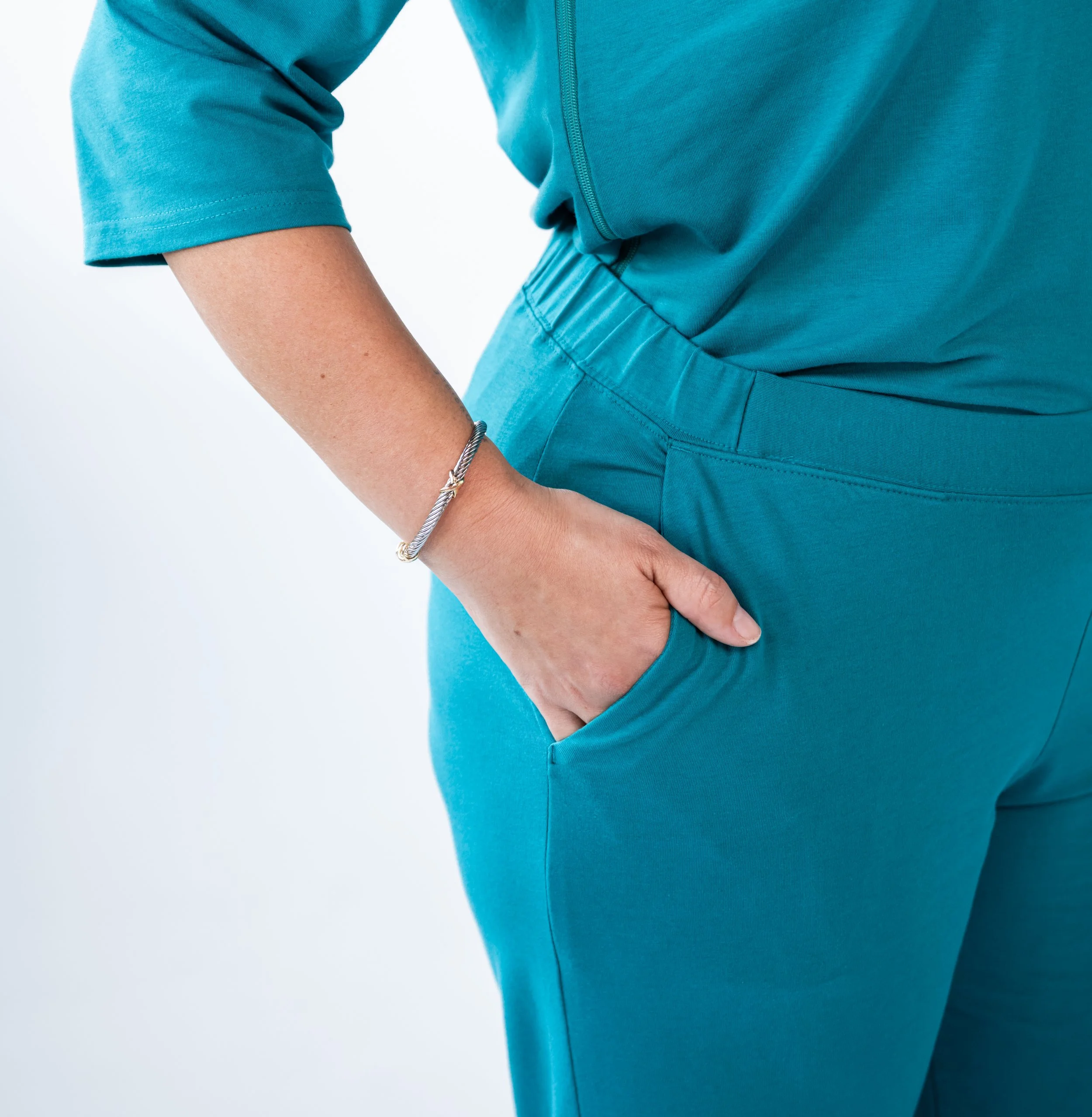 Close-up of a person wearing teal athletic wear with their hand in their pocket, wearing a silver bracelet.