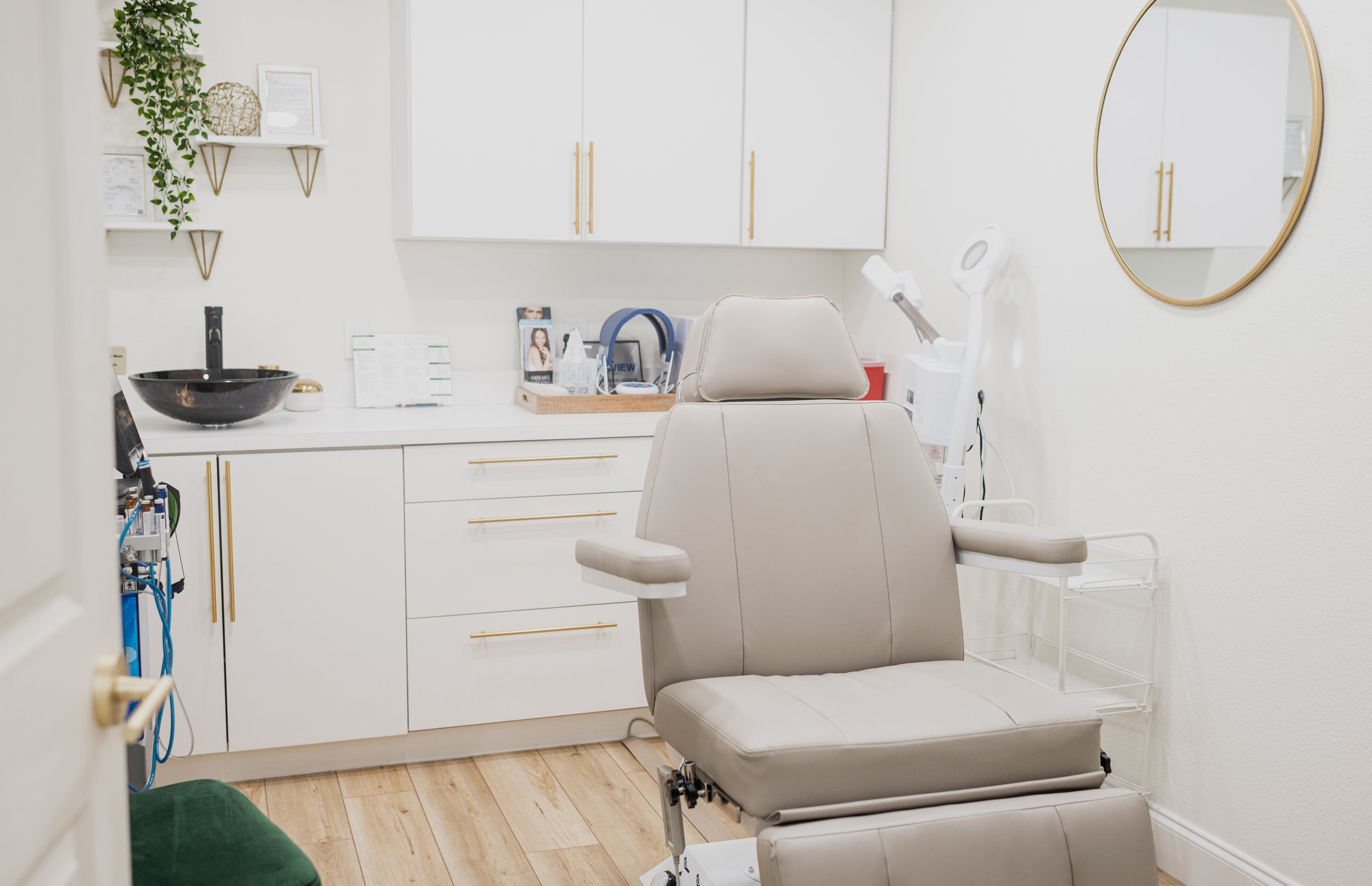 Medical examination room with a beige chair, white cabinets, a round mirror, and medical equipment.