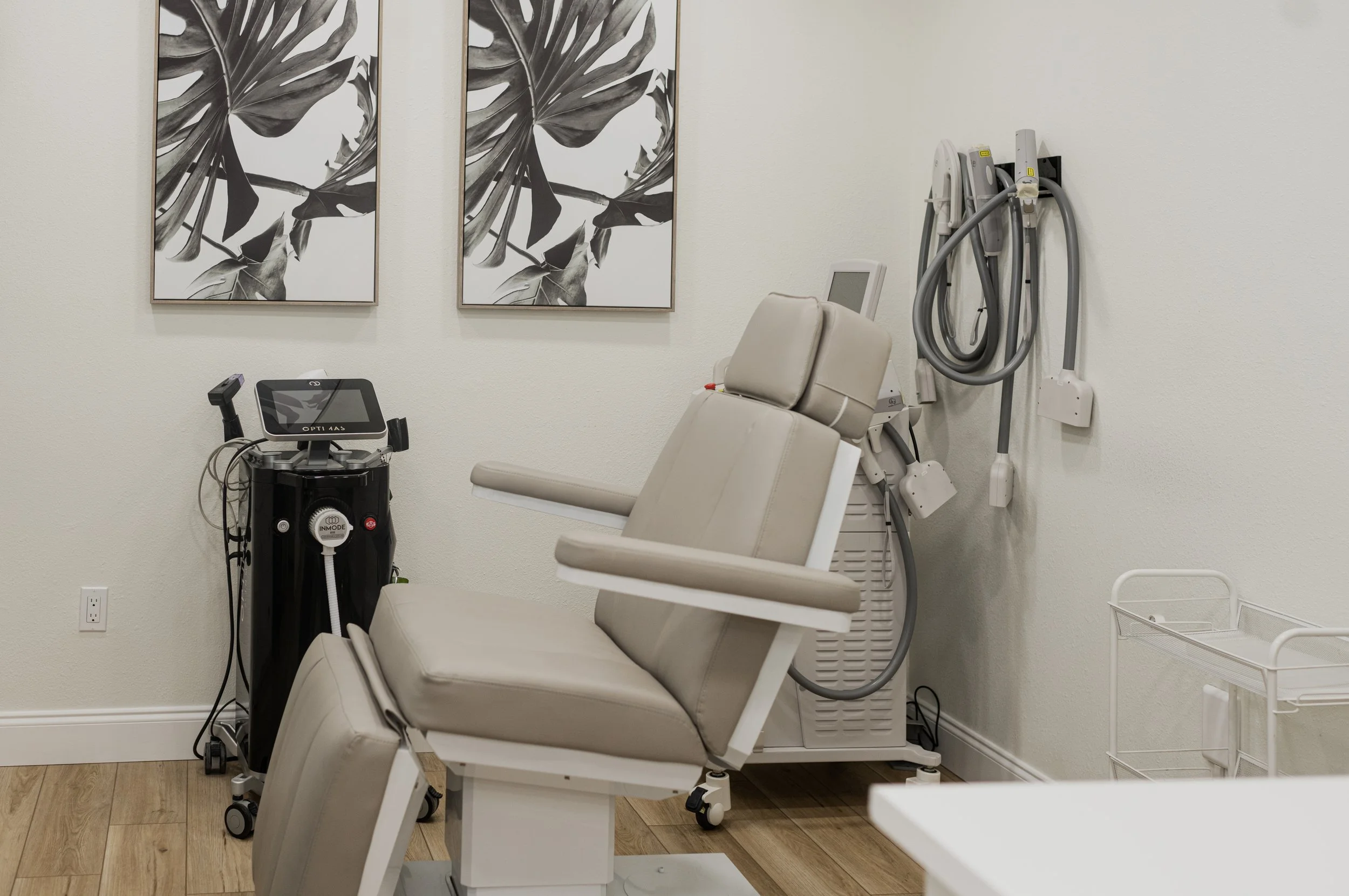 A doctor's examination room with a patient chair, medical equipment, and wall art.