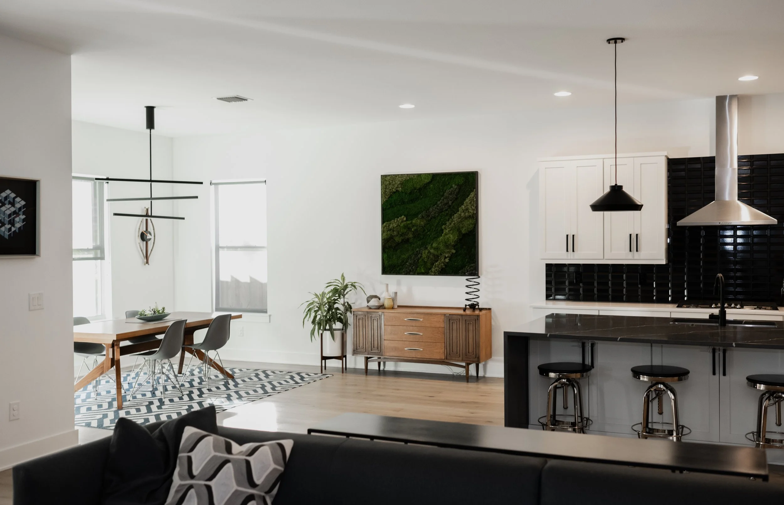 Open-concept living and dining area with a modern kitchen, dining table, black and white decor, and a wall-mounted TV.