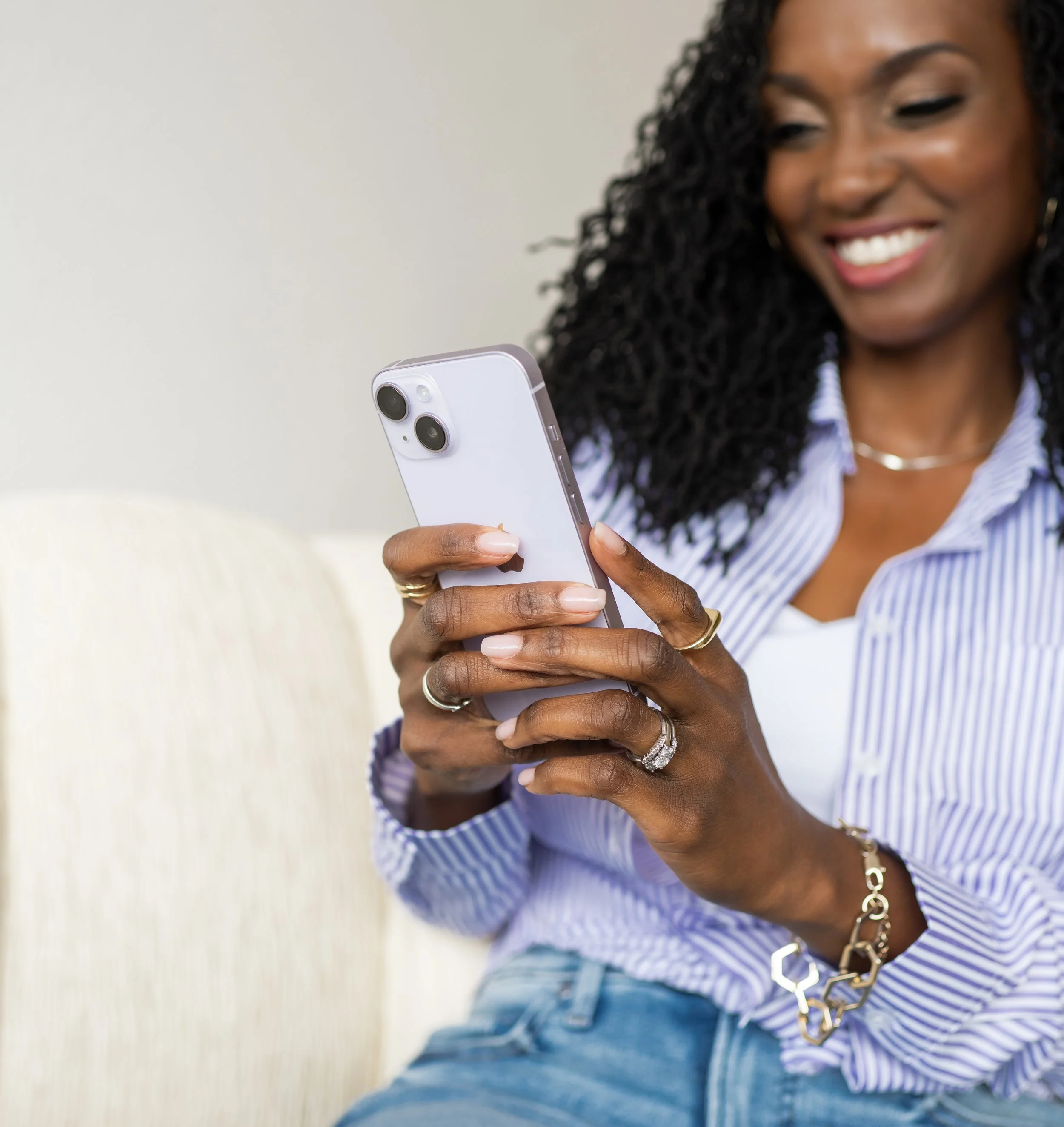 A woman with curly black hair smiling while looking at her phone.