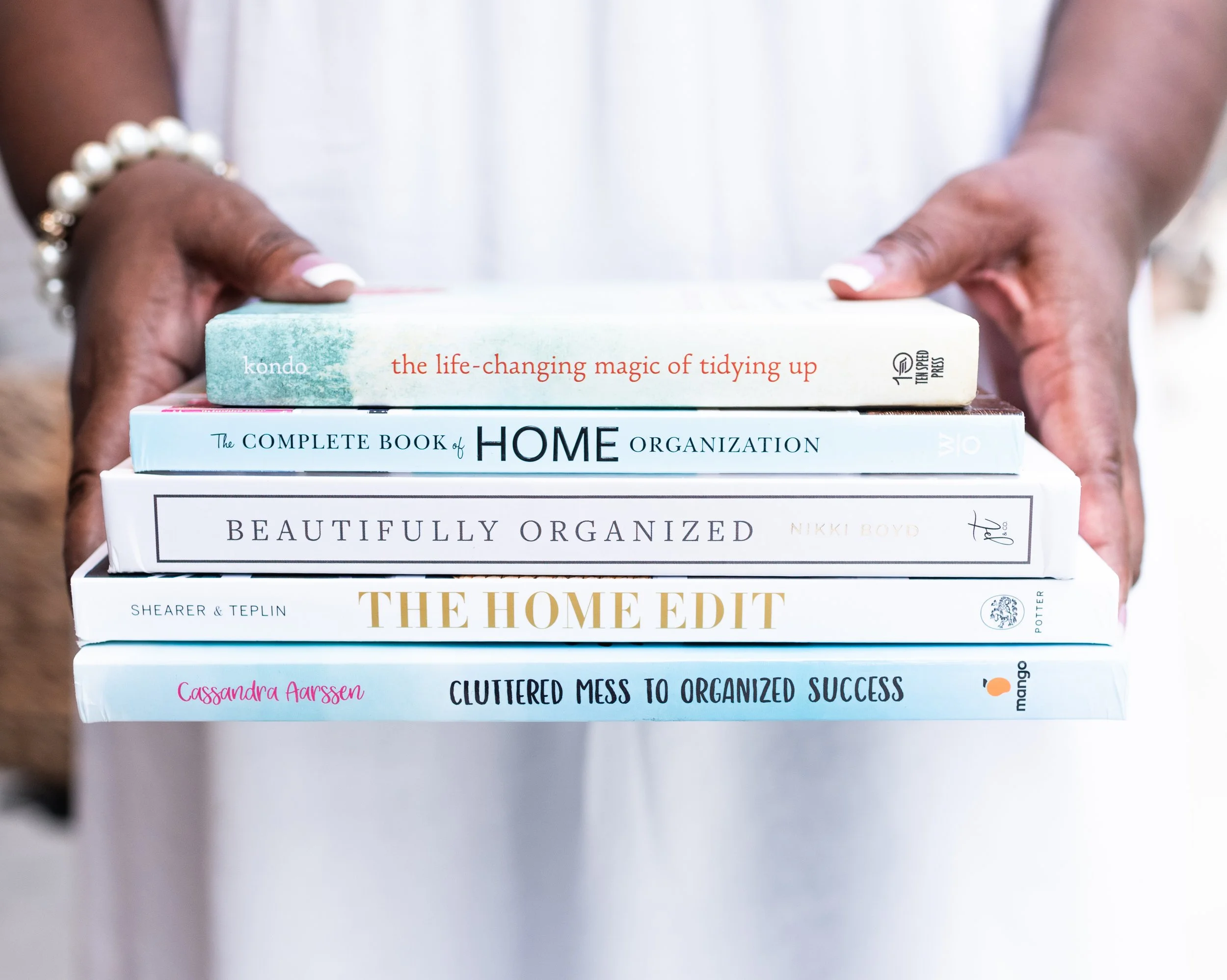 A person holding a stack of six books about organization and home management.