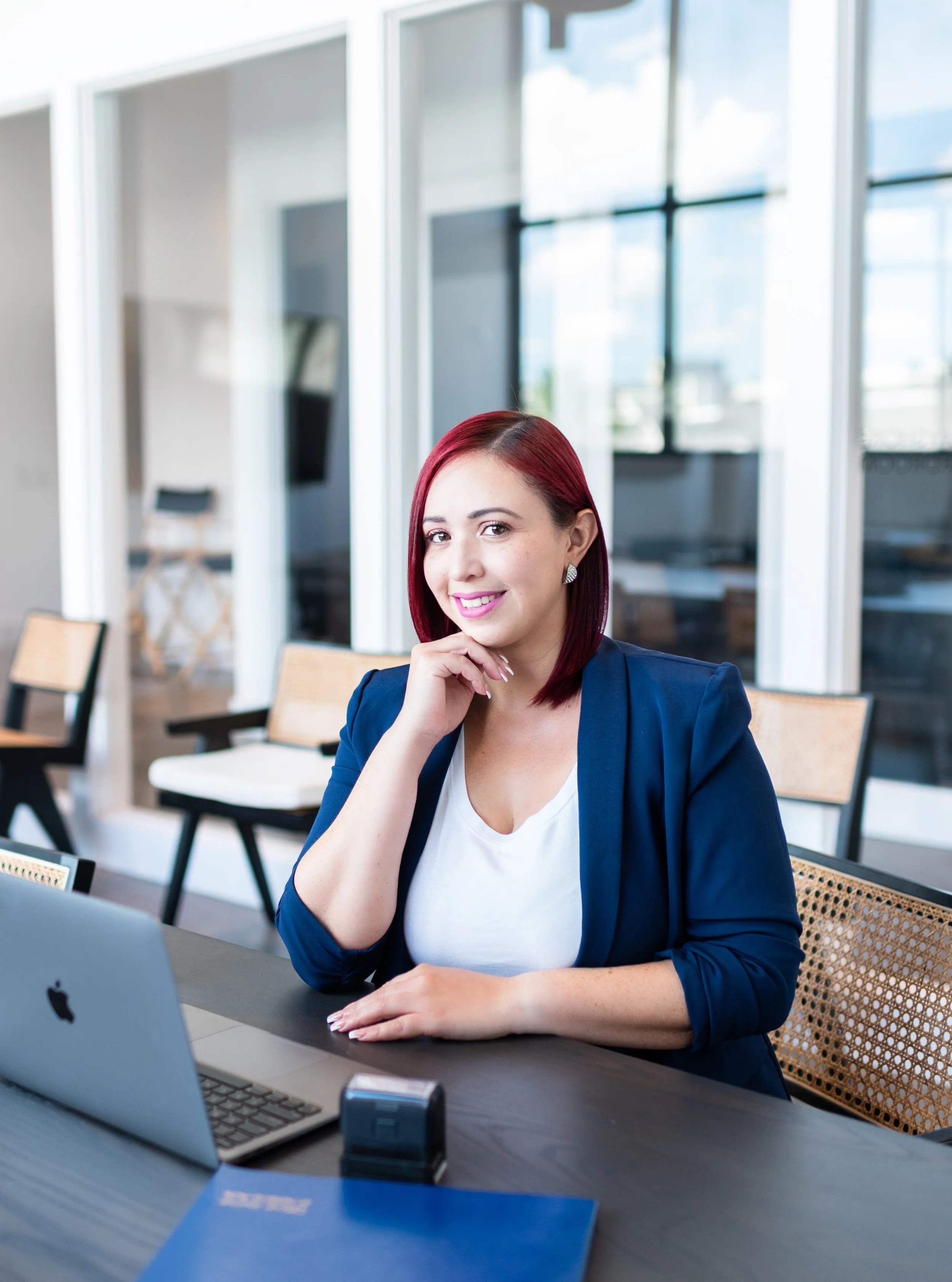 Women with red hair and a blue blazer sitting at a desk in an office.
